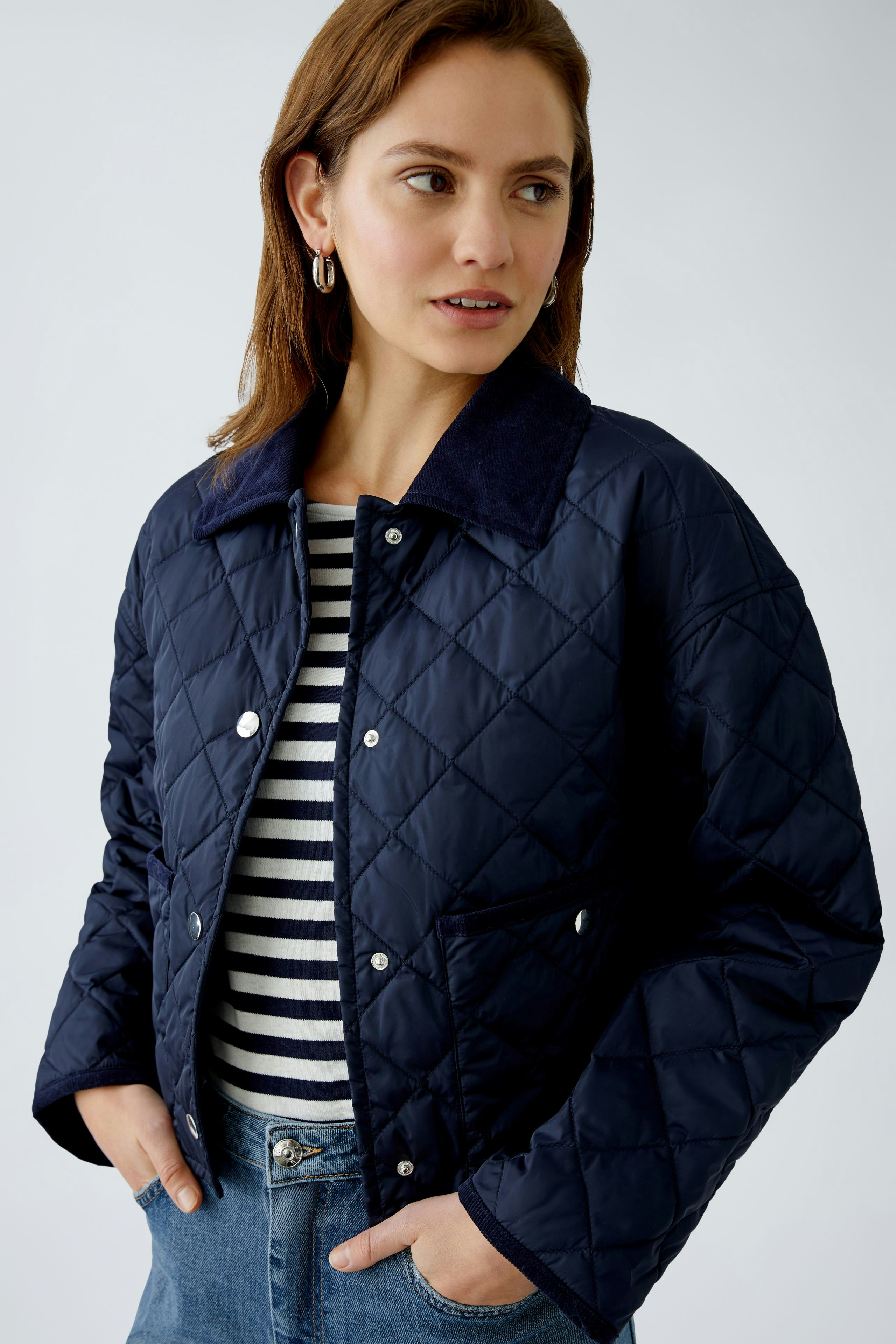 Stylish outdoor jacket: Confident woman in a navy quilted jacket over a striped top.