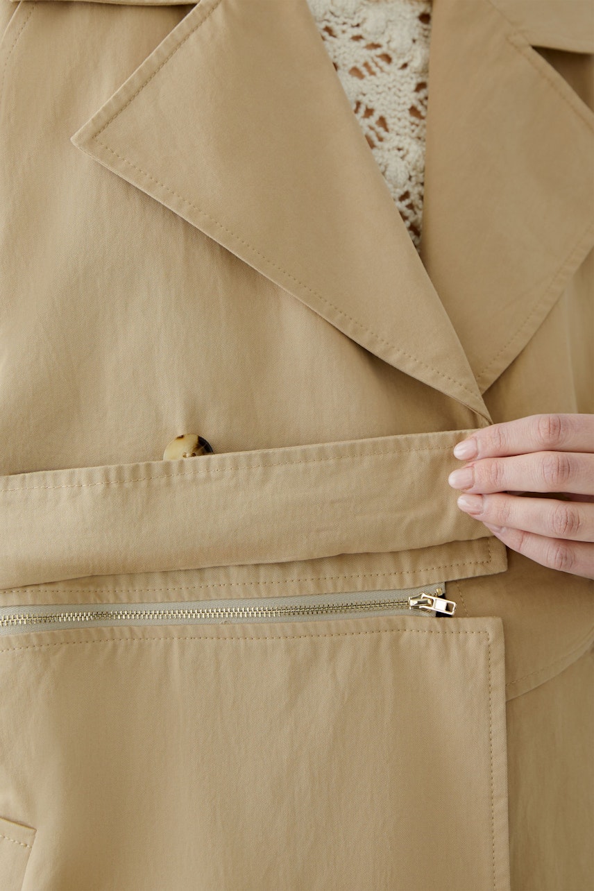 Stylish women's trench coat: Close-up of a woman adjusting the coat's pocket.