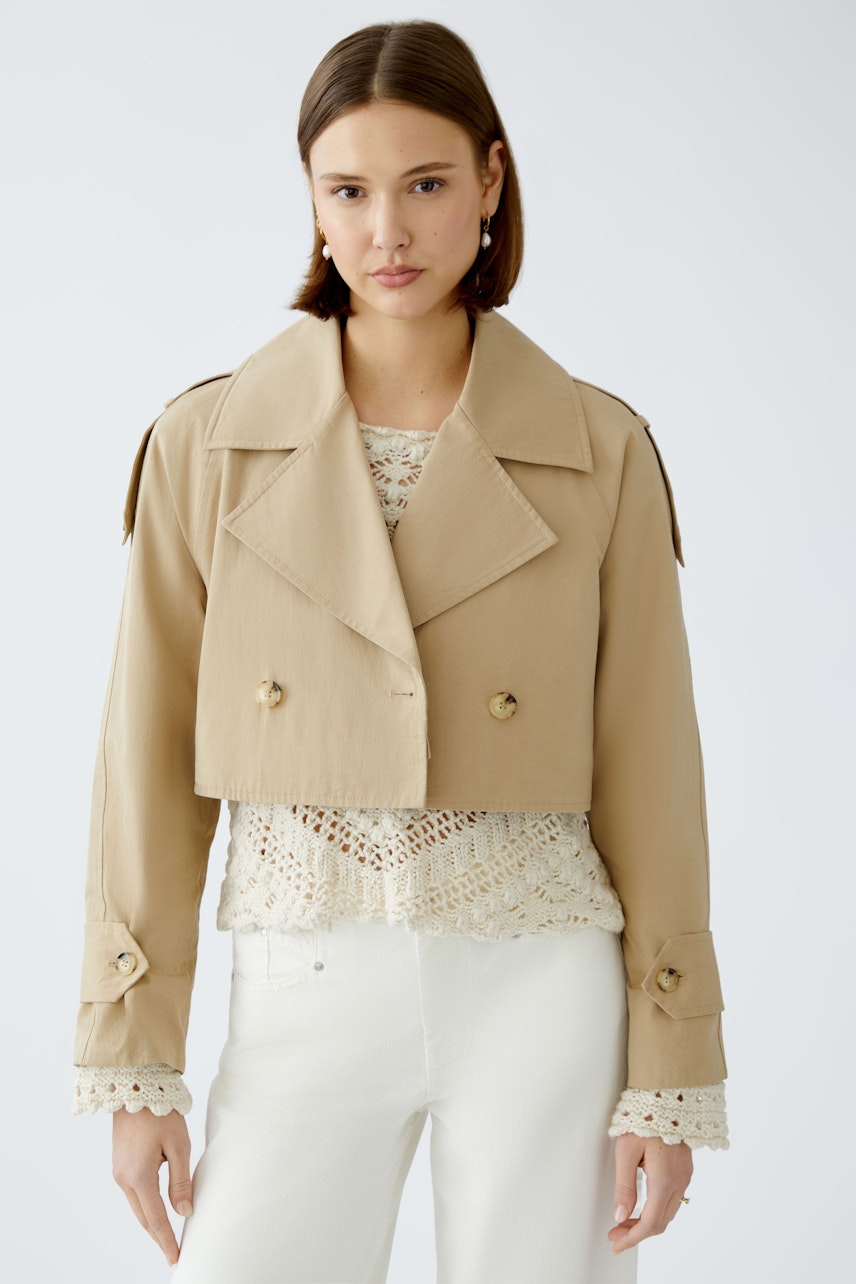 Stylish women's trench coat: A woman in a cropped beige trench coat over a lace top, exuding elegance.