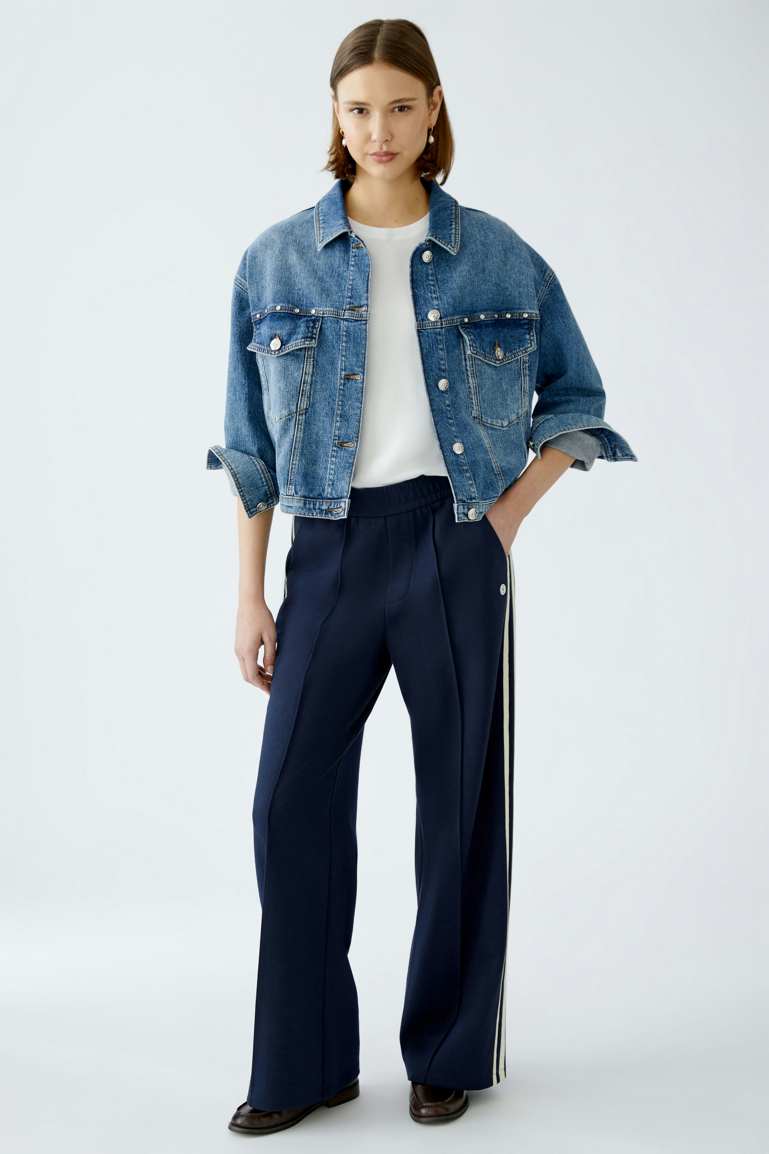Stylish women's trousers: A woman in navy pants with side stripes and a denim jacket stands confidently.