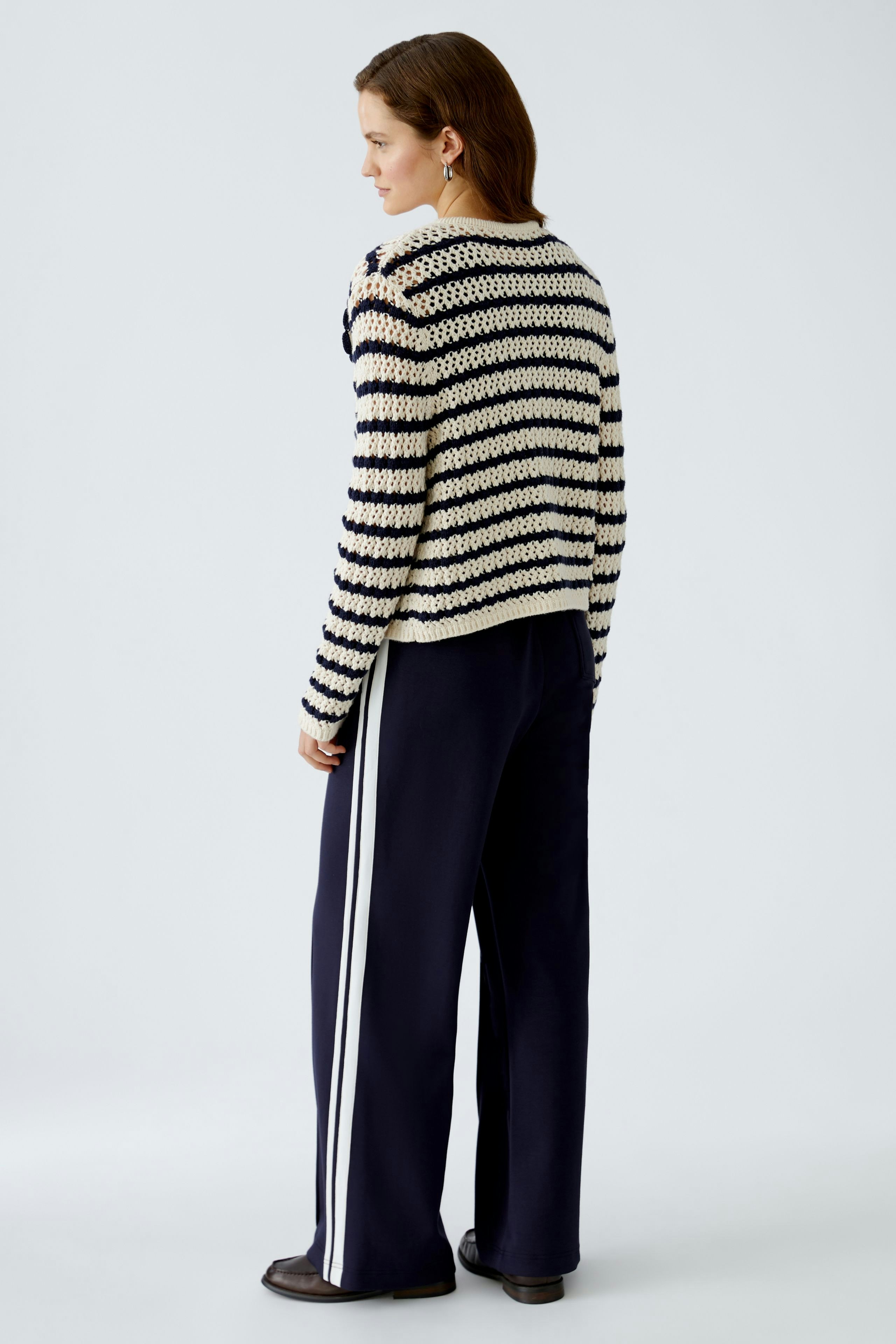 Damen-Strickjacke: Frau in gestreifter Strickjacke mit lässigem Schnitt und bequemen Hosen von hinten.