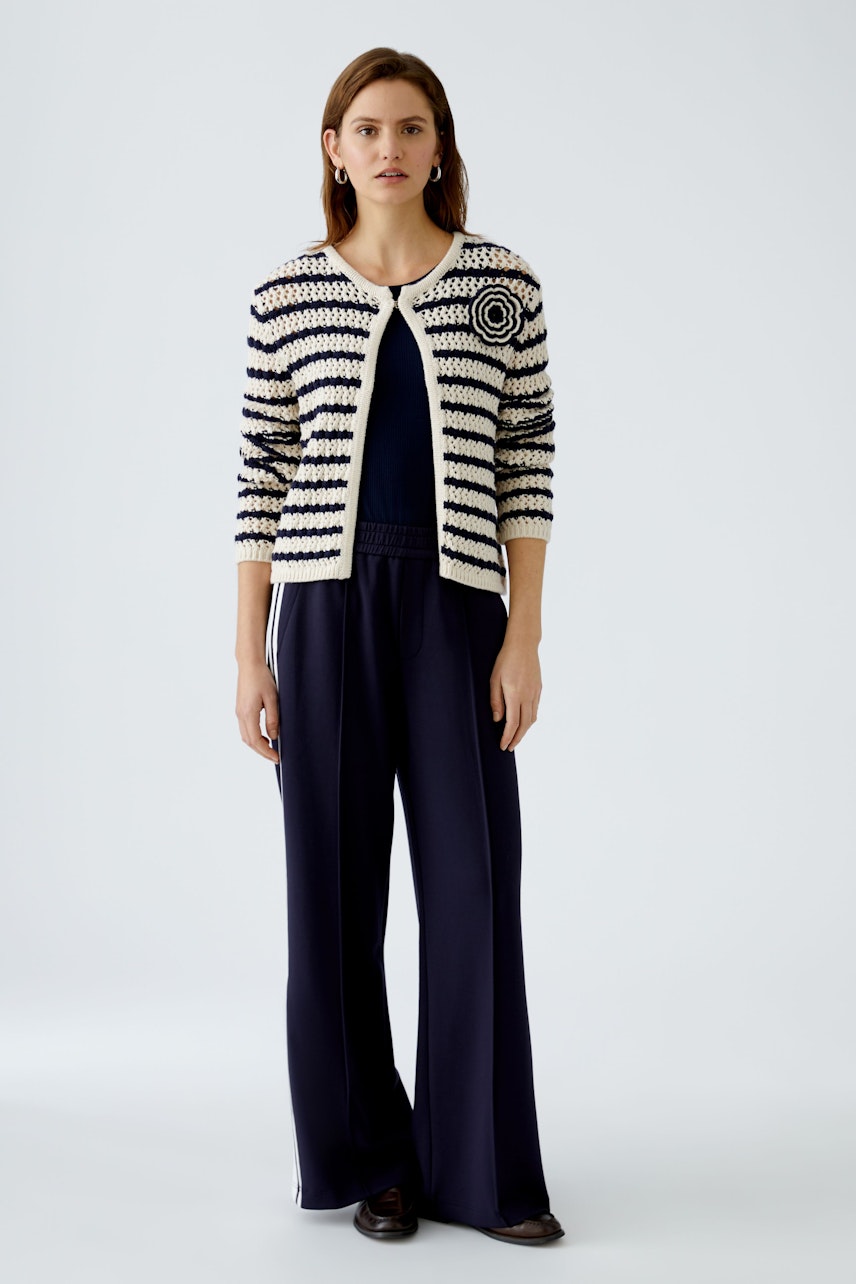 Stylish women's cardigan: A woman in a striped knit cardigan over a navy top and wide-leg pants.