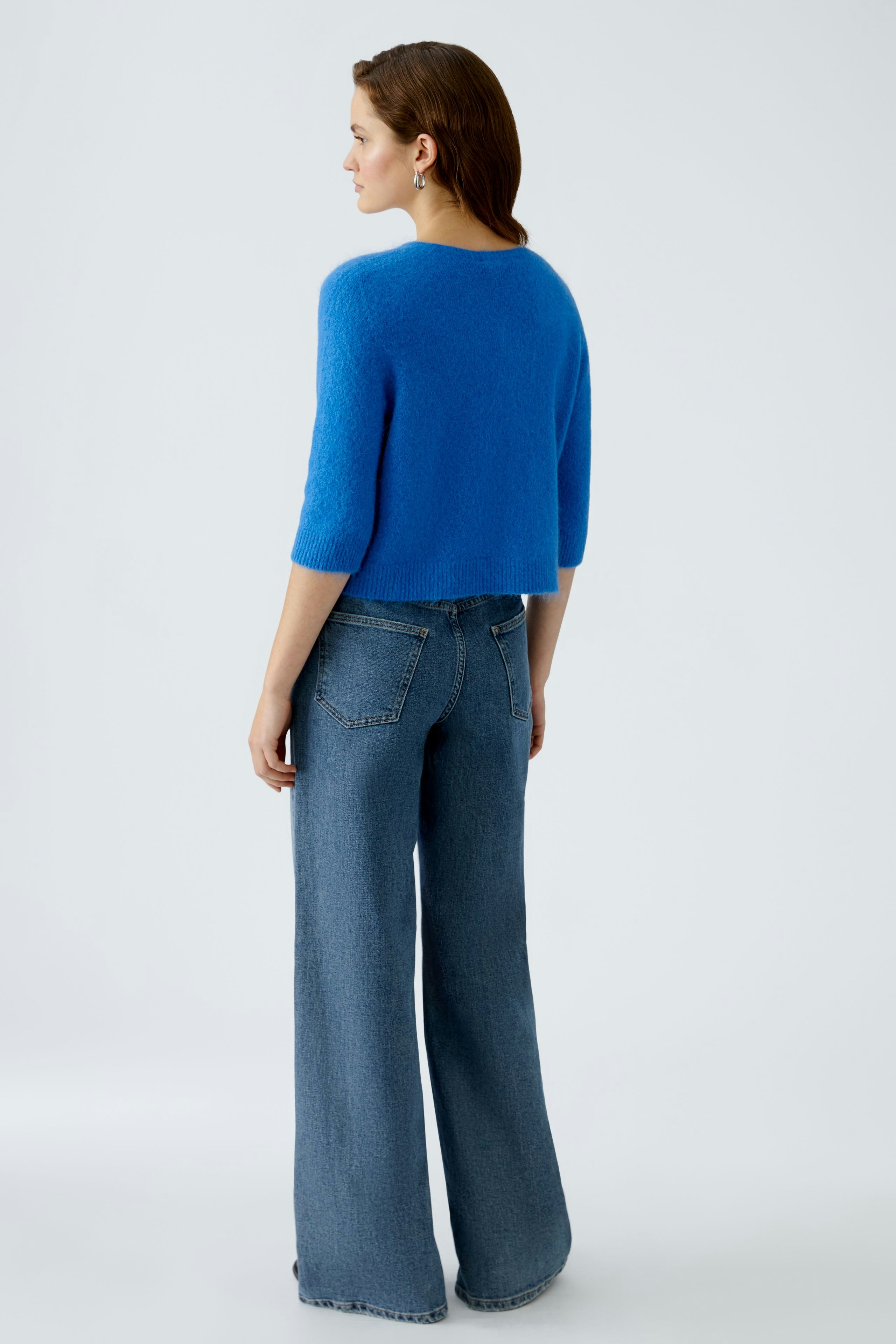 Damen-Strickjacke: Frau in blauer Strickjacke mit kurzen Ärmeln und lässigen Jeans von hinten.