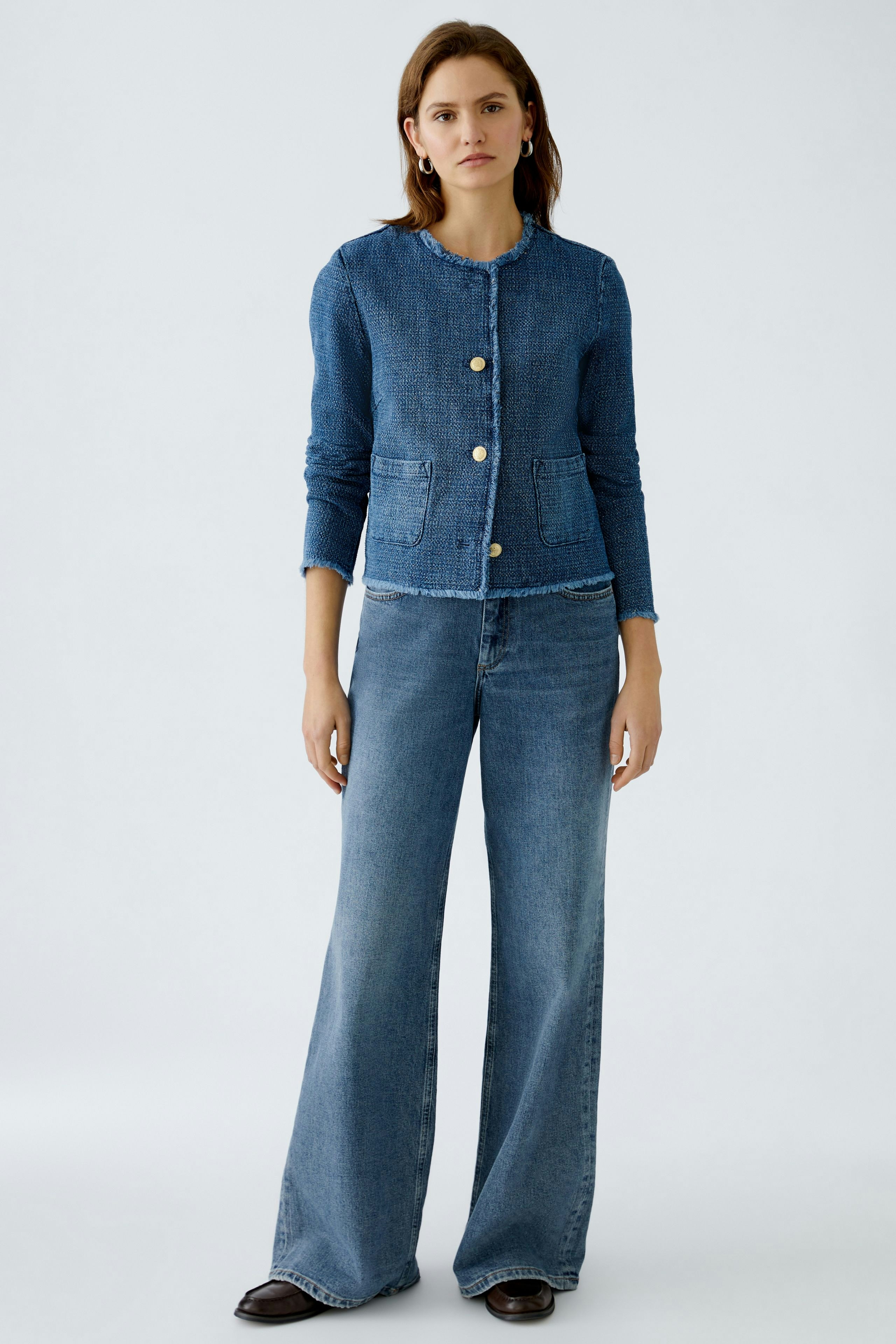 Chic women's jacket: A woman in a blue textured jacket with buttons and pockets, paired with flared jeans.