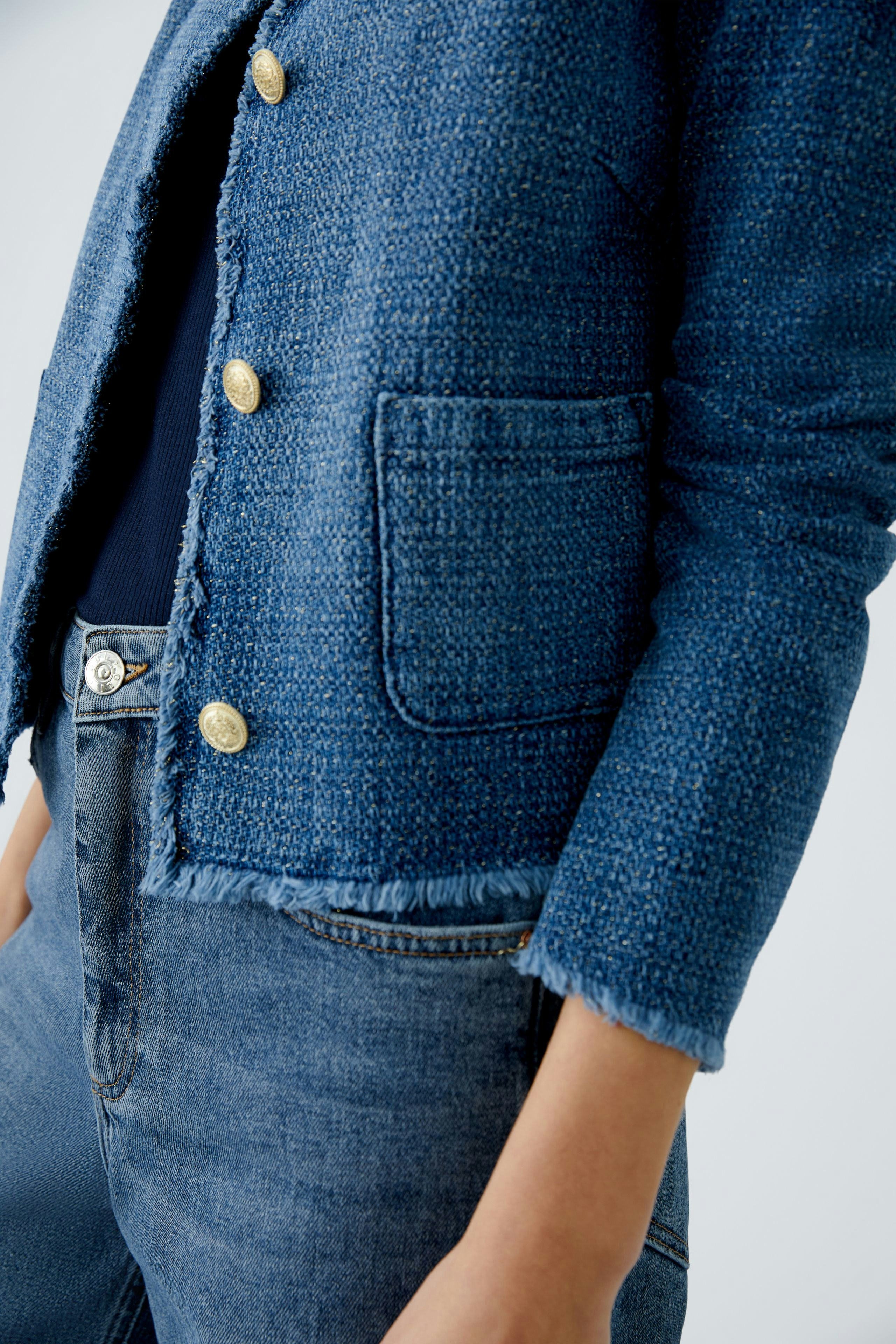 Stylish women's jacket: A woman in a blue textured jacket with gold buttons and a casual look.