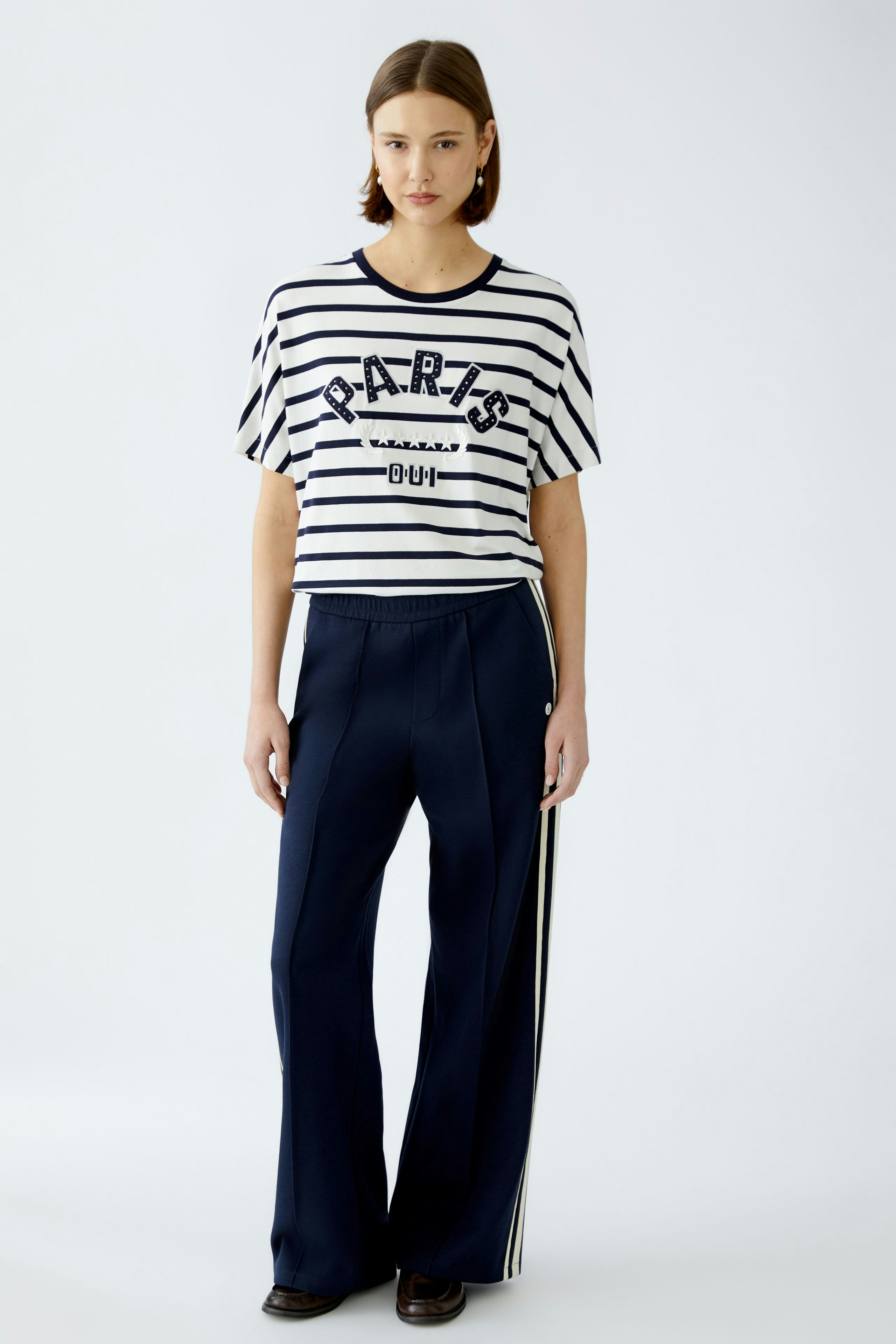Stylish women's T-shirt: A woman in a striped tee with 'PARIS' print, paired with navy pants.