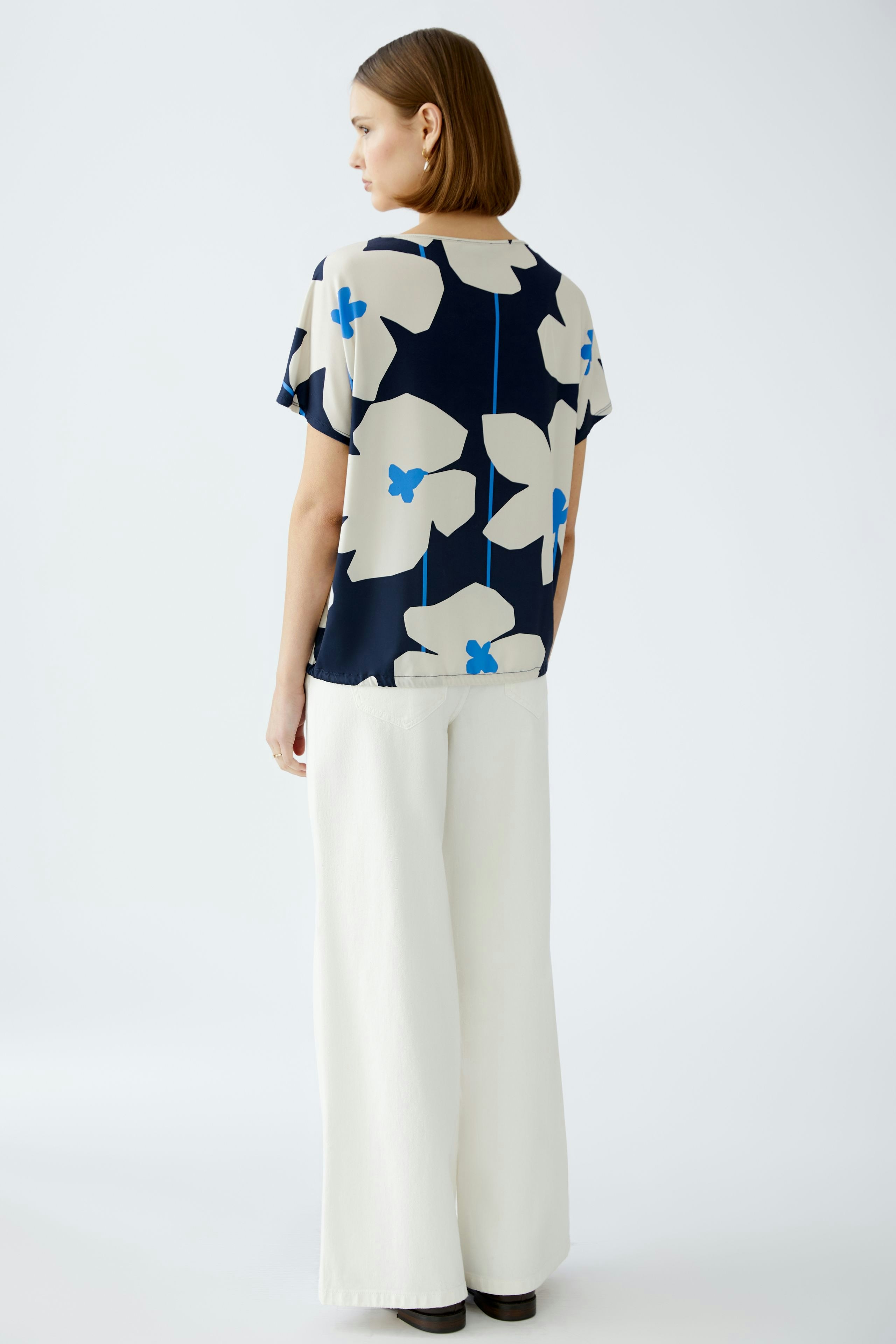 Damen-T-Shirt: Frau trägt ein blumiges, navyfarbenes T-Shirt mit lockerer Passform und weiten Hosen.
