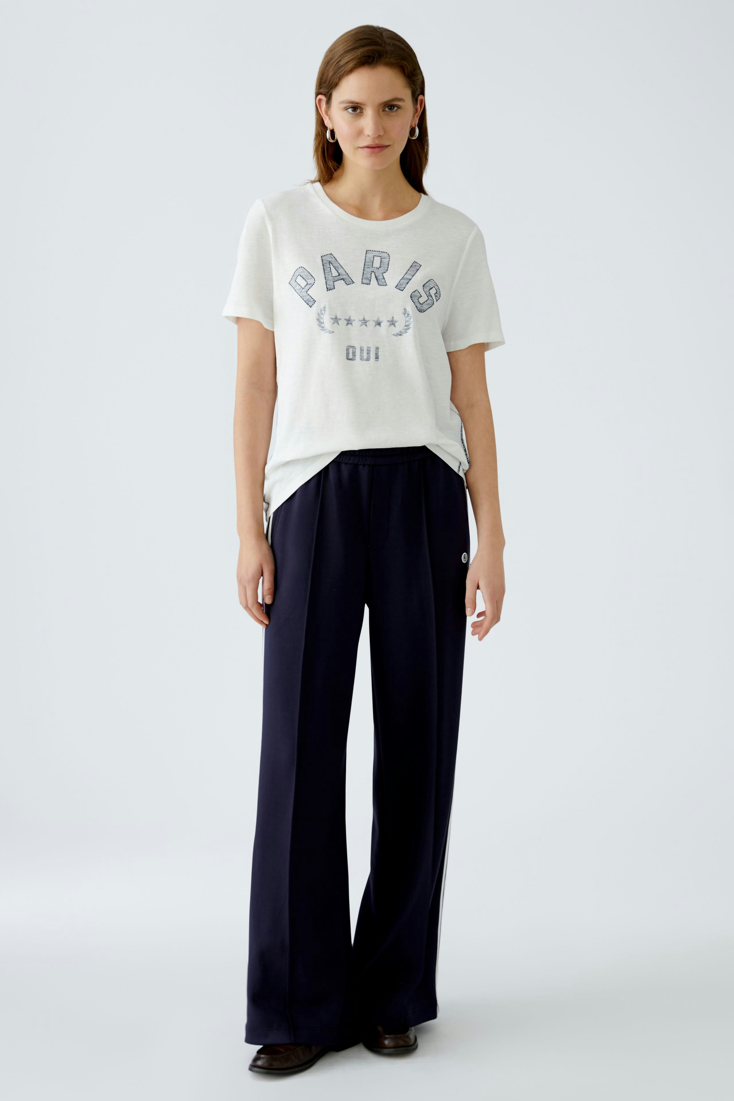 Casual women's T-shirt: Young woman in a white tee with 'PARIS' print and relaxed fit.