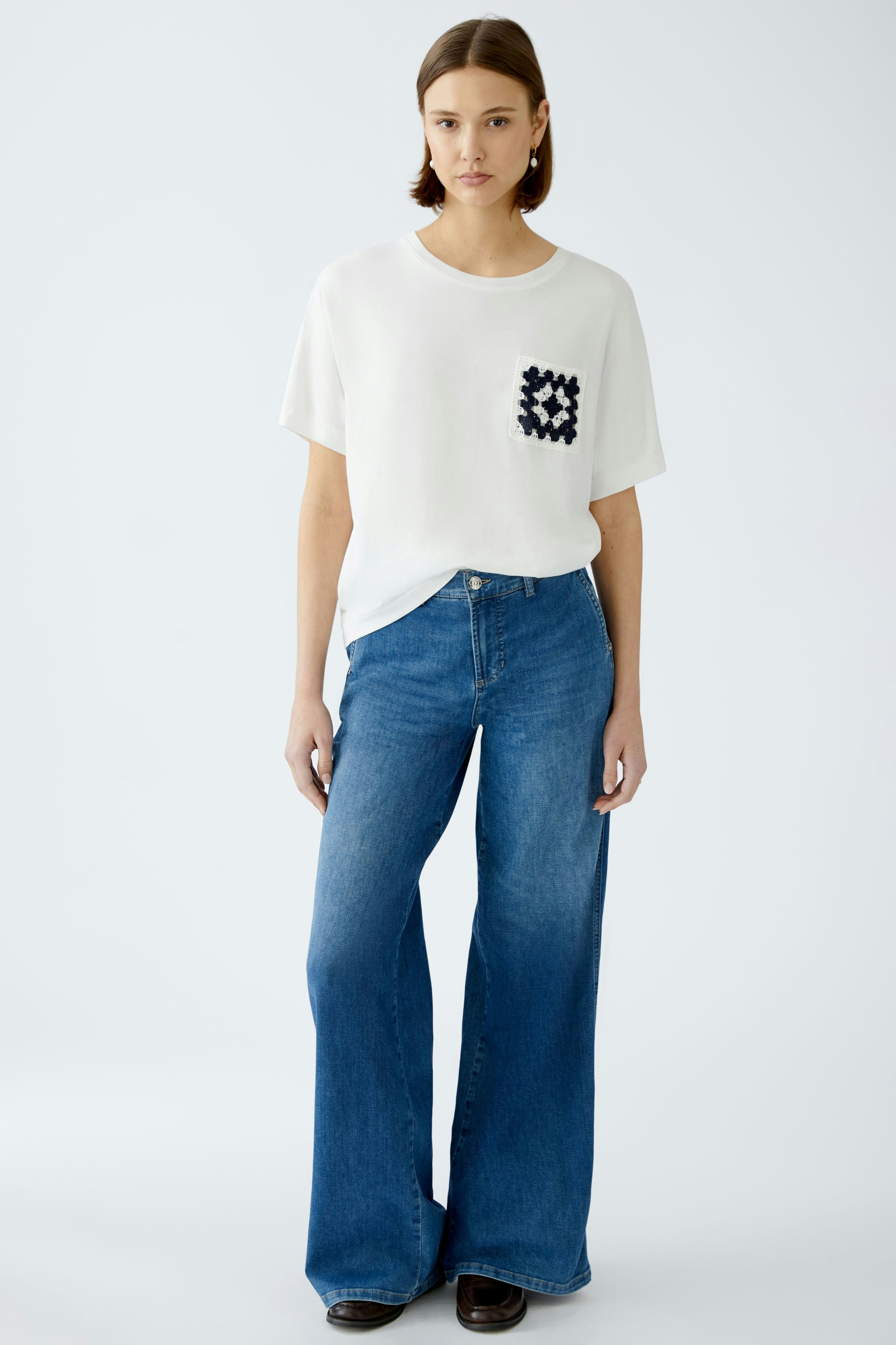 Stylish women's T-shirt: A woman in a white tee with a pocket detail, paired with flared jeans.