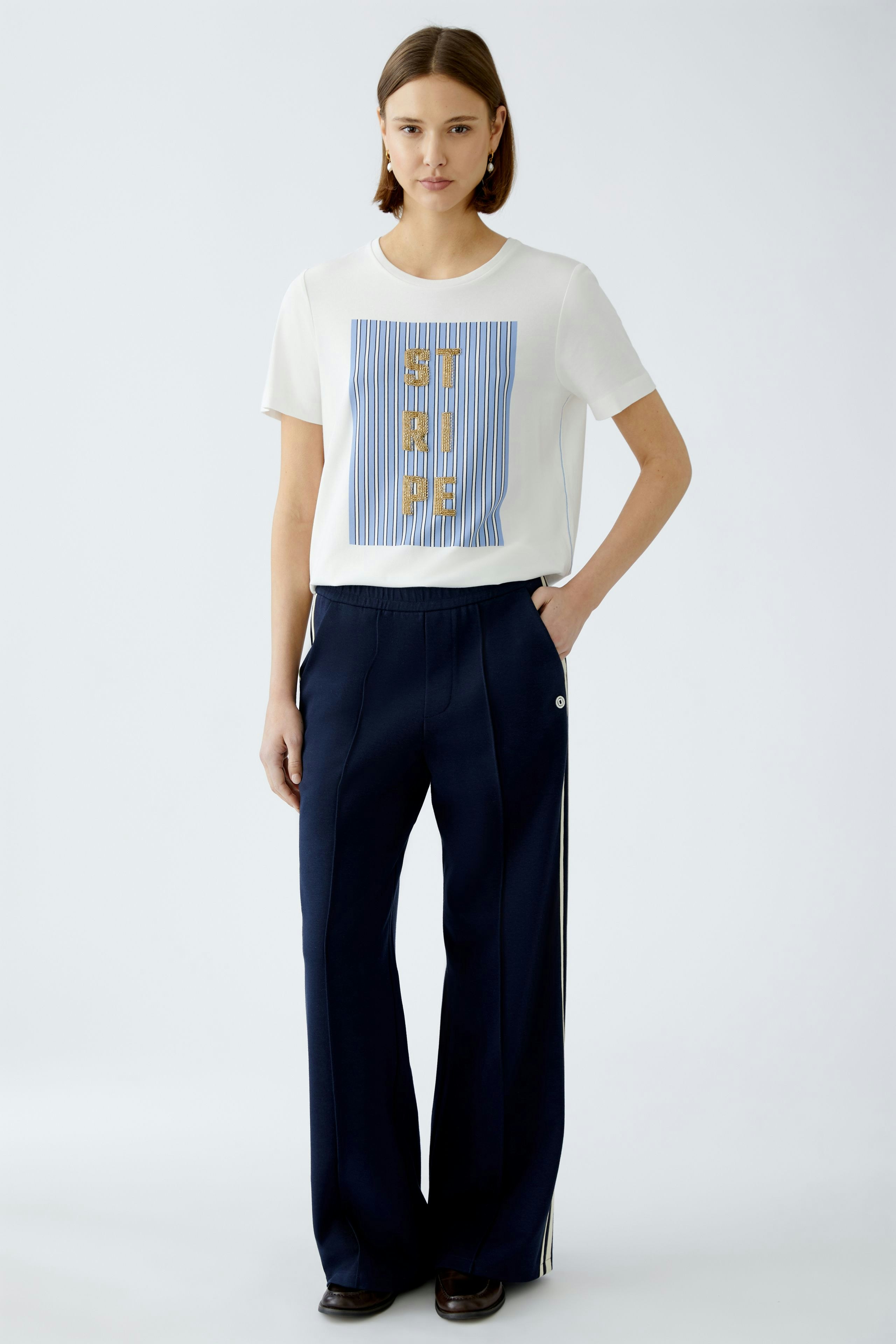 Stylish women's T-shirt: A woman in a white tee with a graphic print, paired with navy trousers.