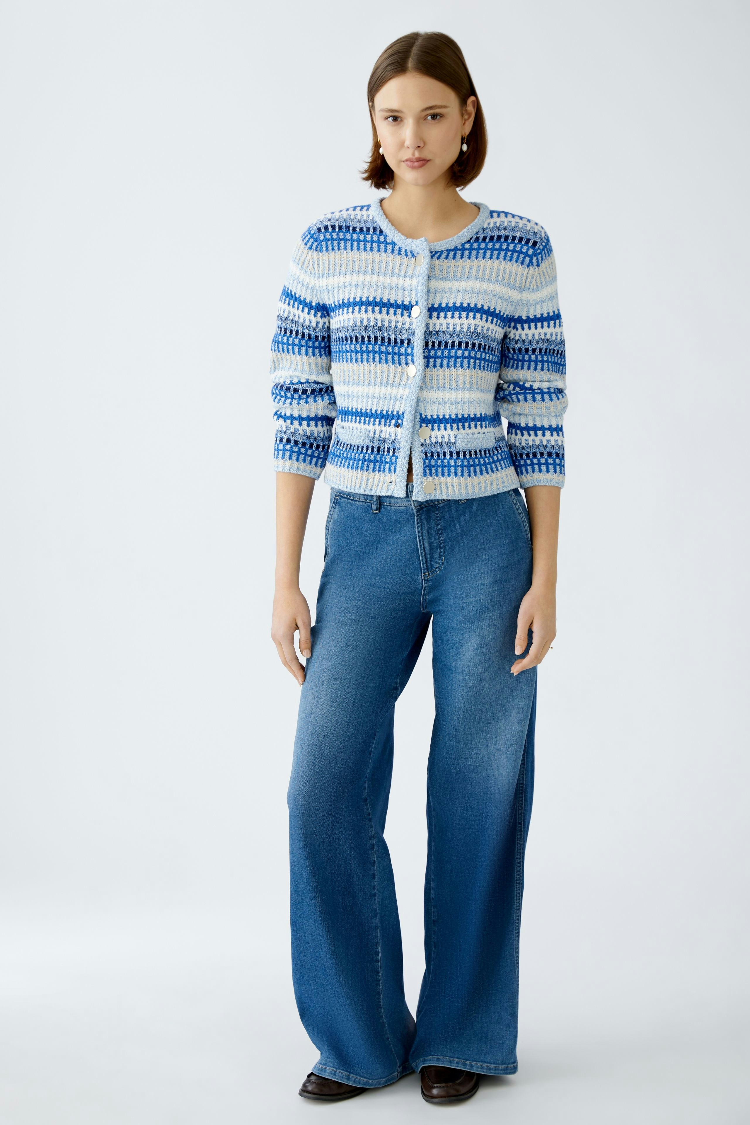 Stylish women's cardigan: A woman in a blue patterned cardigan paired with flared jeans.