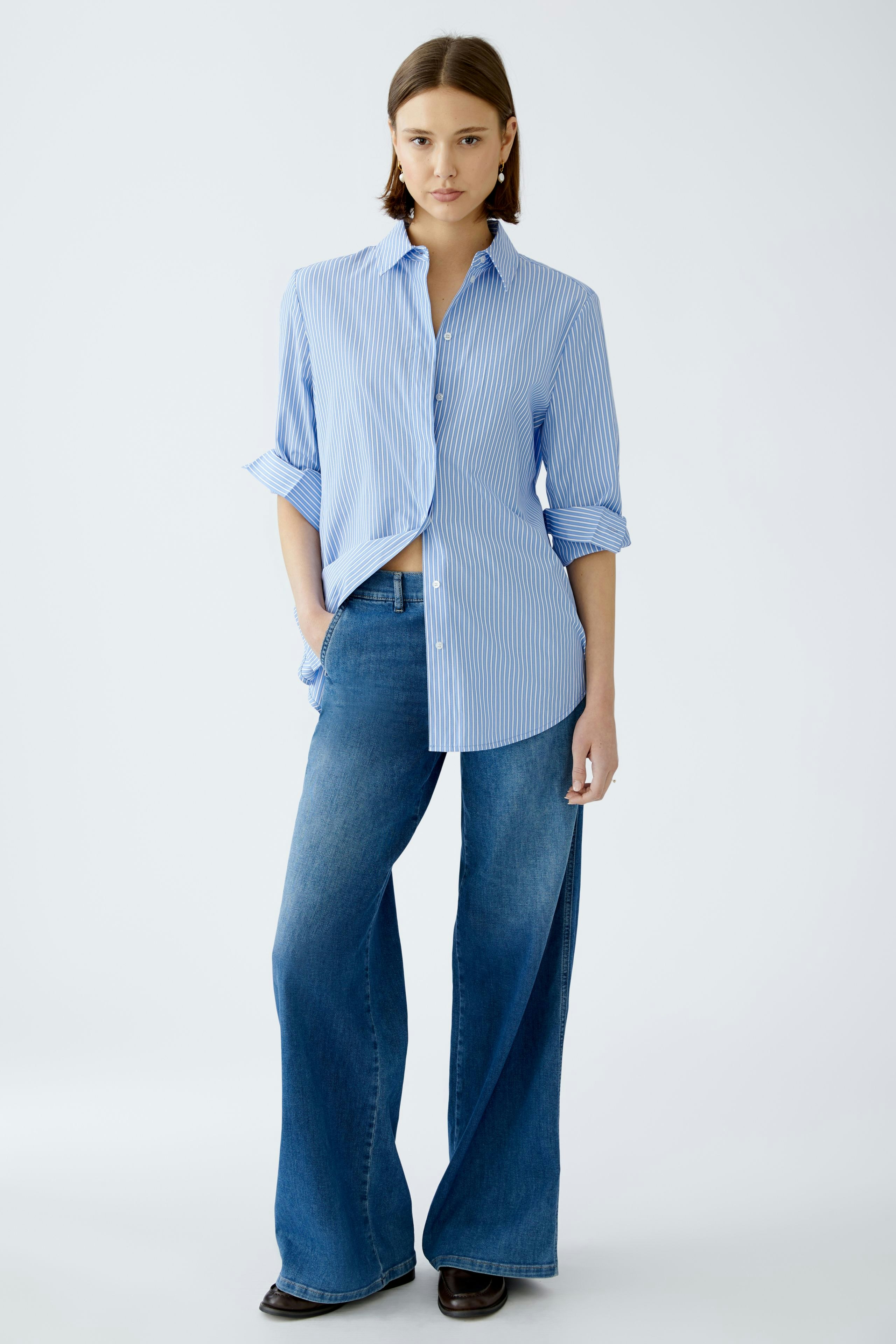 Stylish women's blouse: A woman in a blue striped shirt paired with wide-leg jeans.