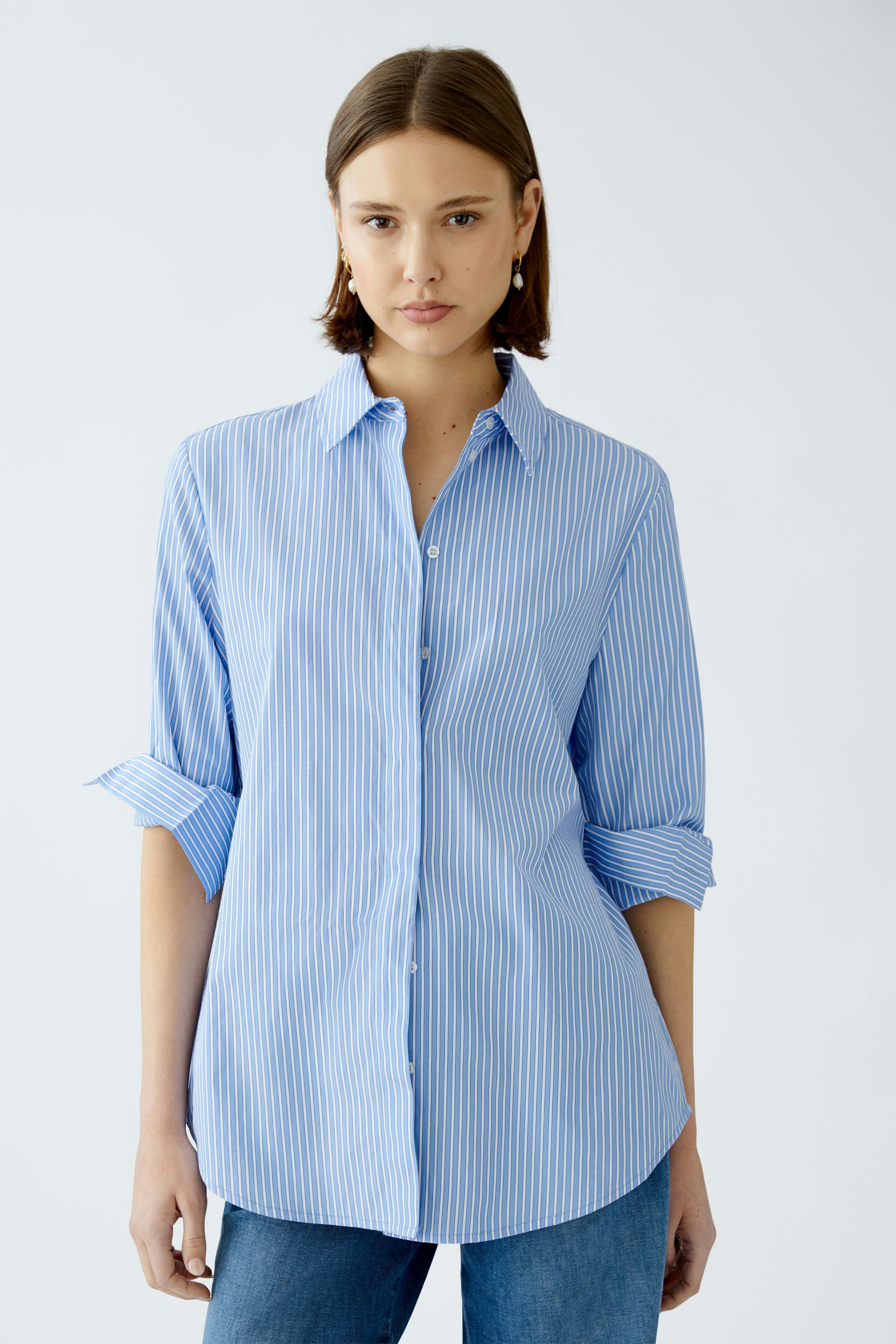 Stylish women's blouse: A woman in a light blue striped blouse with rolled-up sleeves.