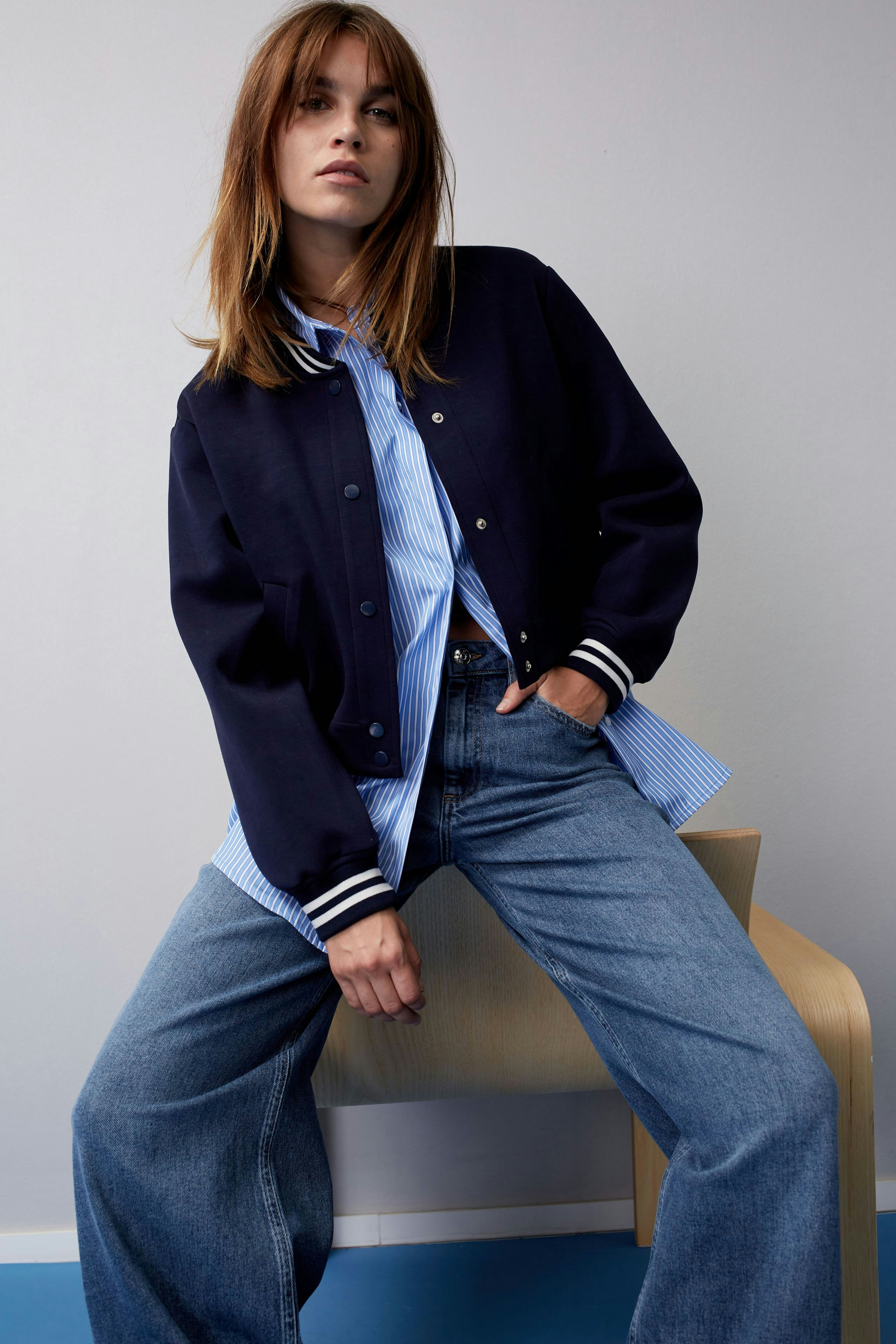 Stylish women's blouse: A woman in a blue striped blouse layered under a navy bomber jacket.