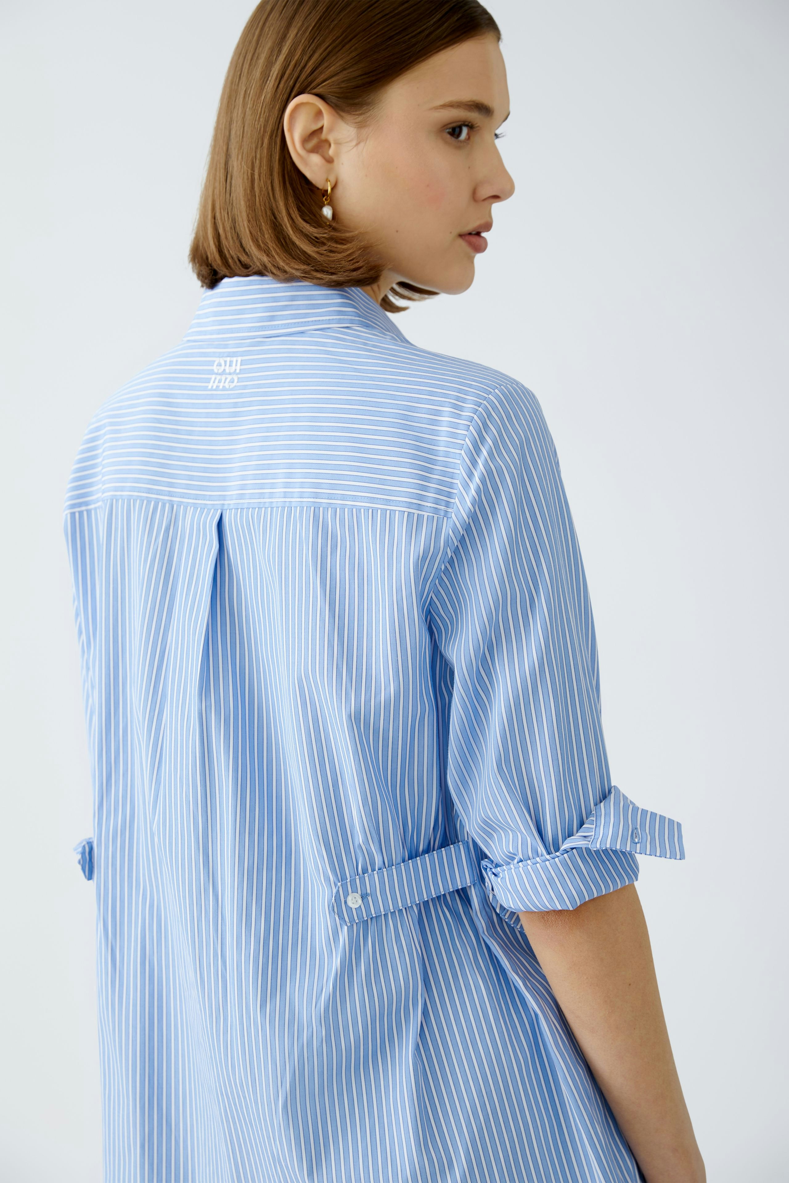 Stylish women's blouse: A woman in a blue striped blouse with rolled sleeves, exuding elegance.