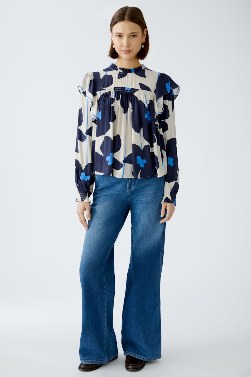 Stylish blouse: Woman in a floral-patterned blouse with ruffled sleeves and relaxed fit jeans.