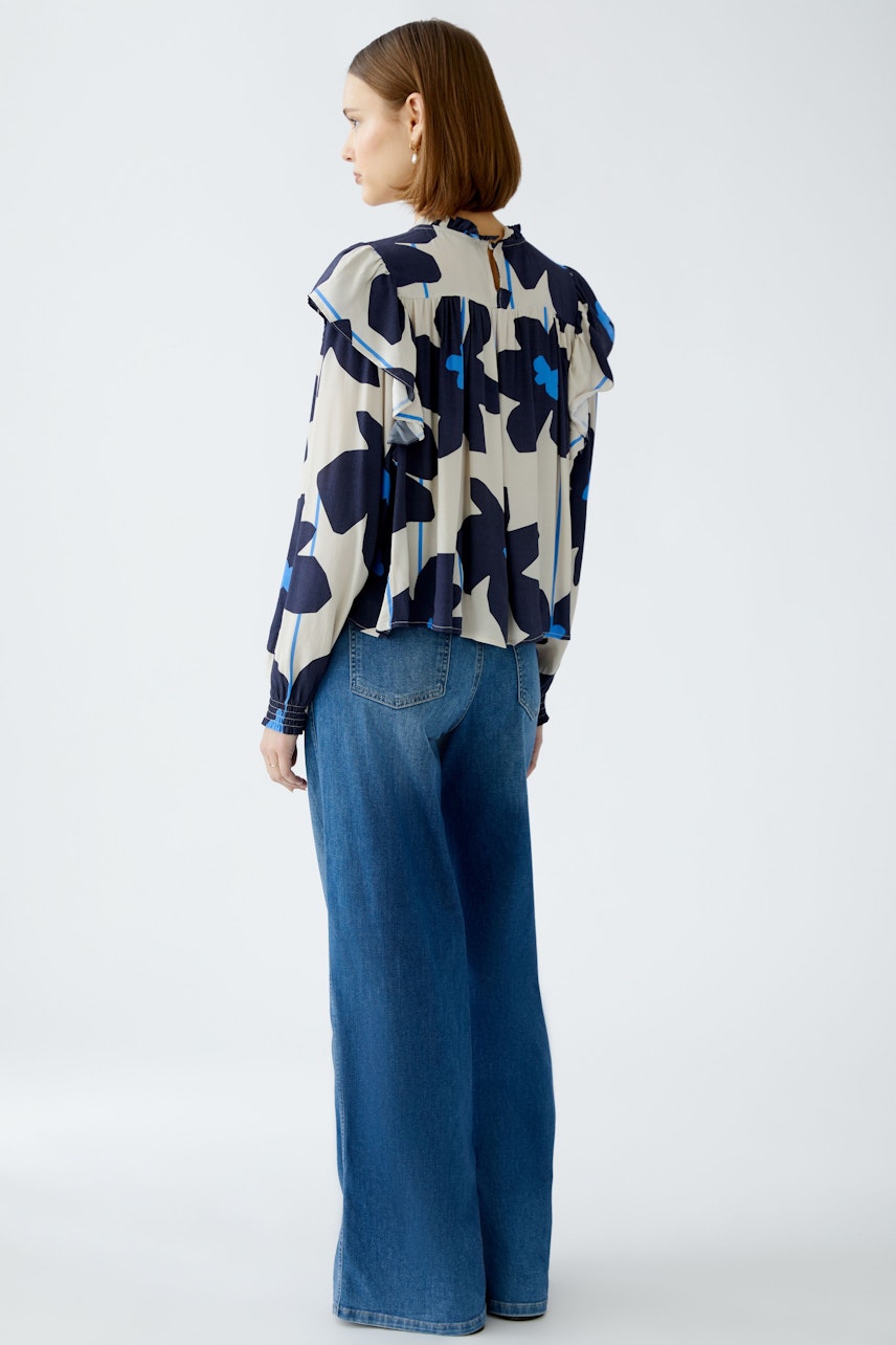 Stylish blouse: Woman in a floral-patterned blouse with ruffles, paired with wide-leg jeans.