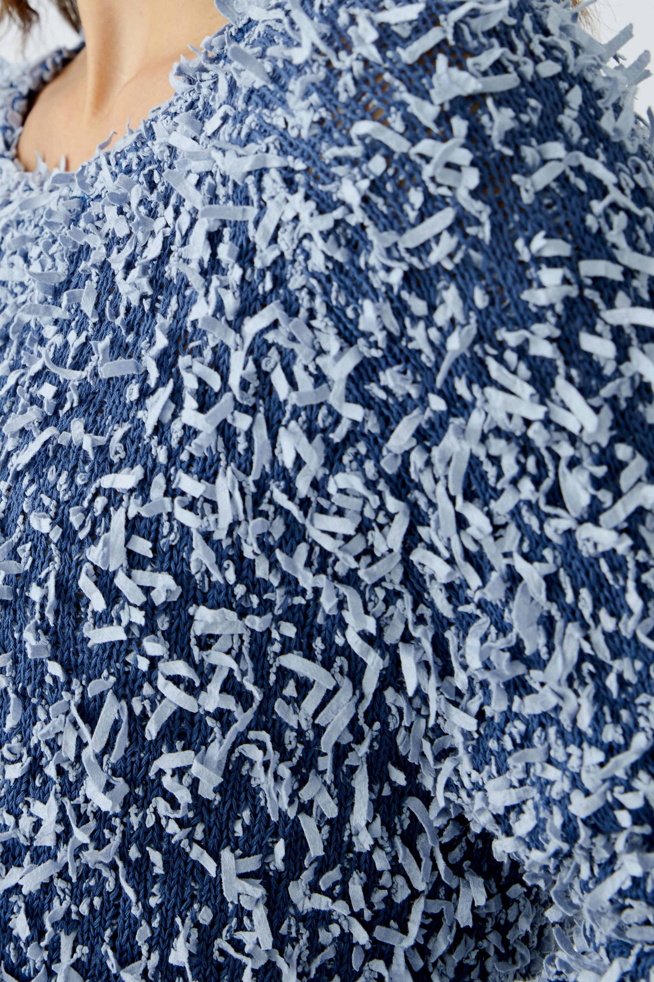 Textured blue pullover: A woman showcases a cozy, stylish pullover with unique frayed detailing.