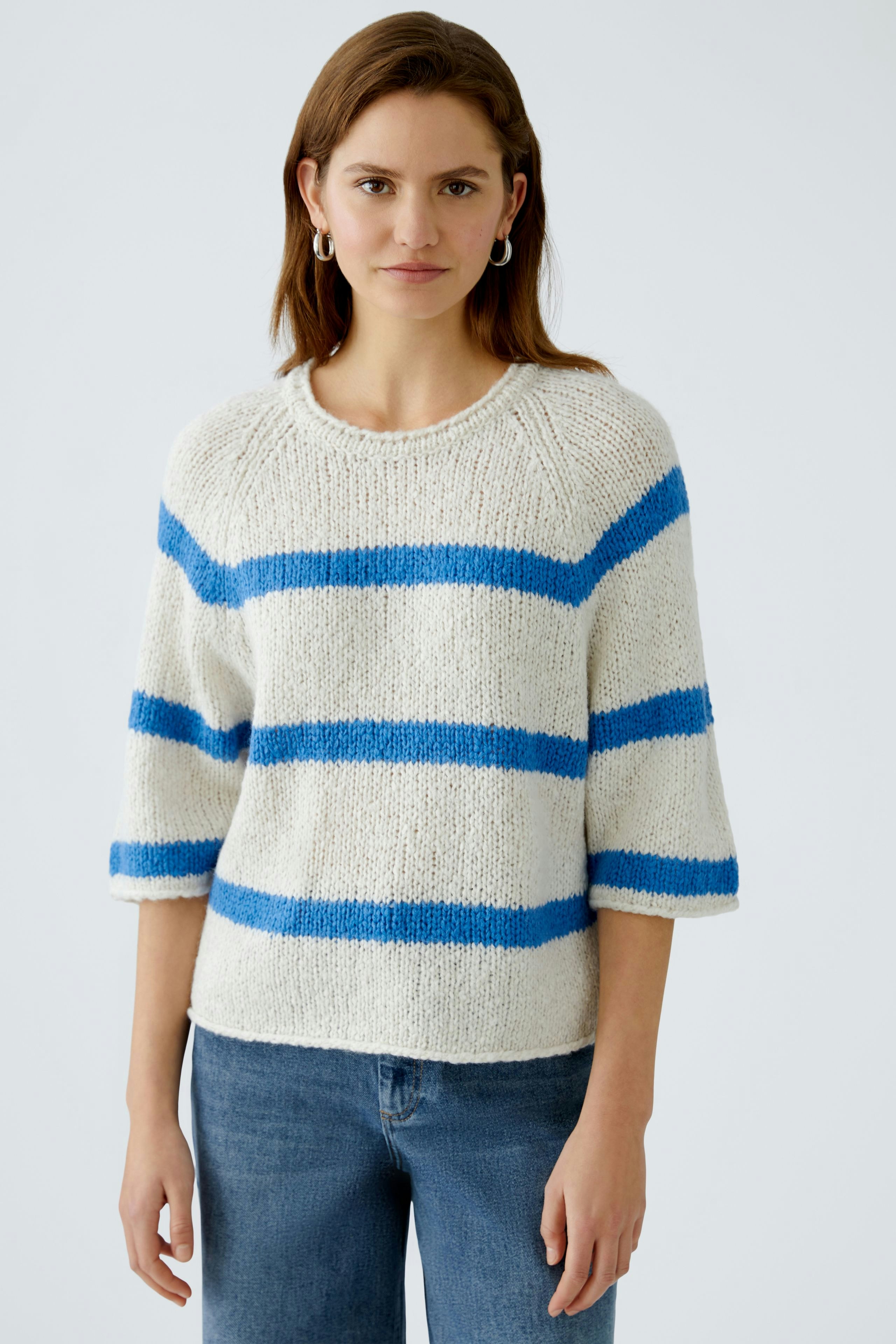 Damen-Pullover: Junge Frau in einem gestreiften, hellen Pullover mit blauen Streifen und lässigen Jeans.