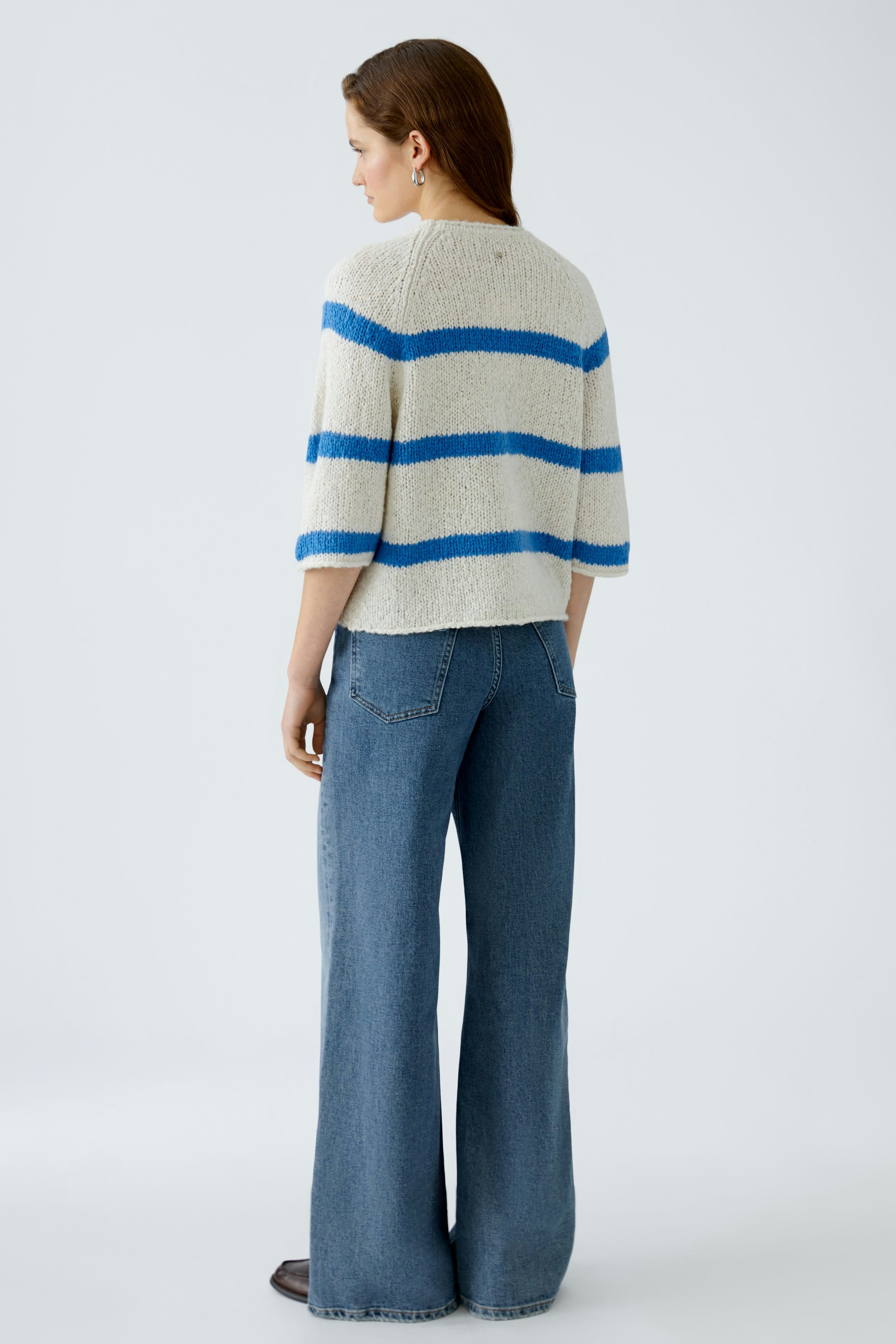 Damen-Pullover: Frau trägt einen beigen Pullover mit blauen Streifen und lässigen Jeans.