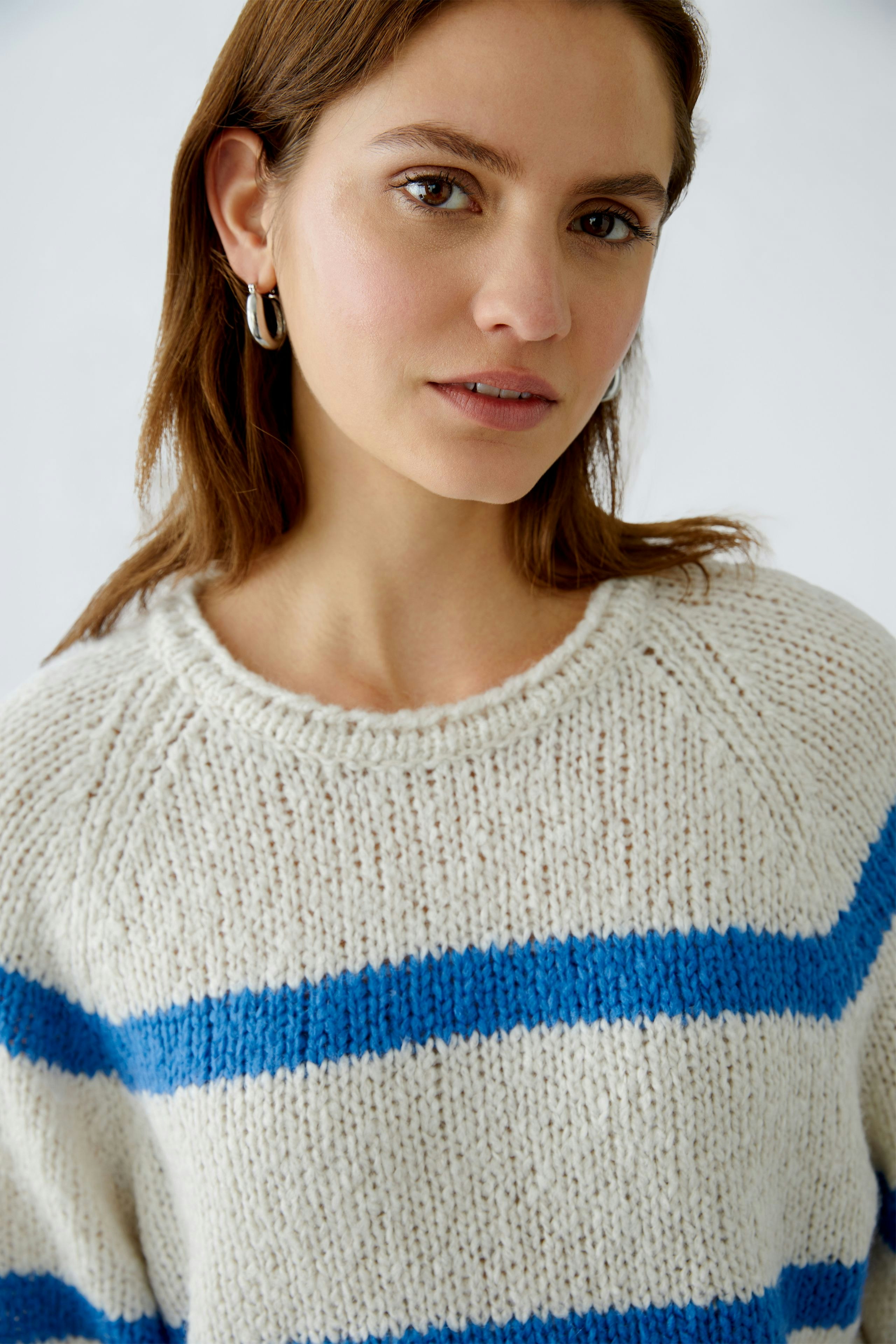 Damen-Pullover: Junge Frau trägt einen beigen Pullover mit blauen Streifen und lässigem Look.