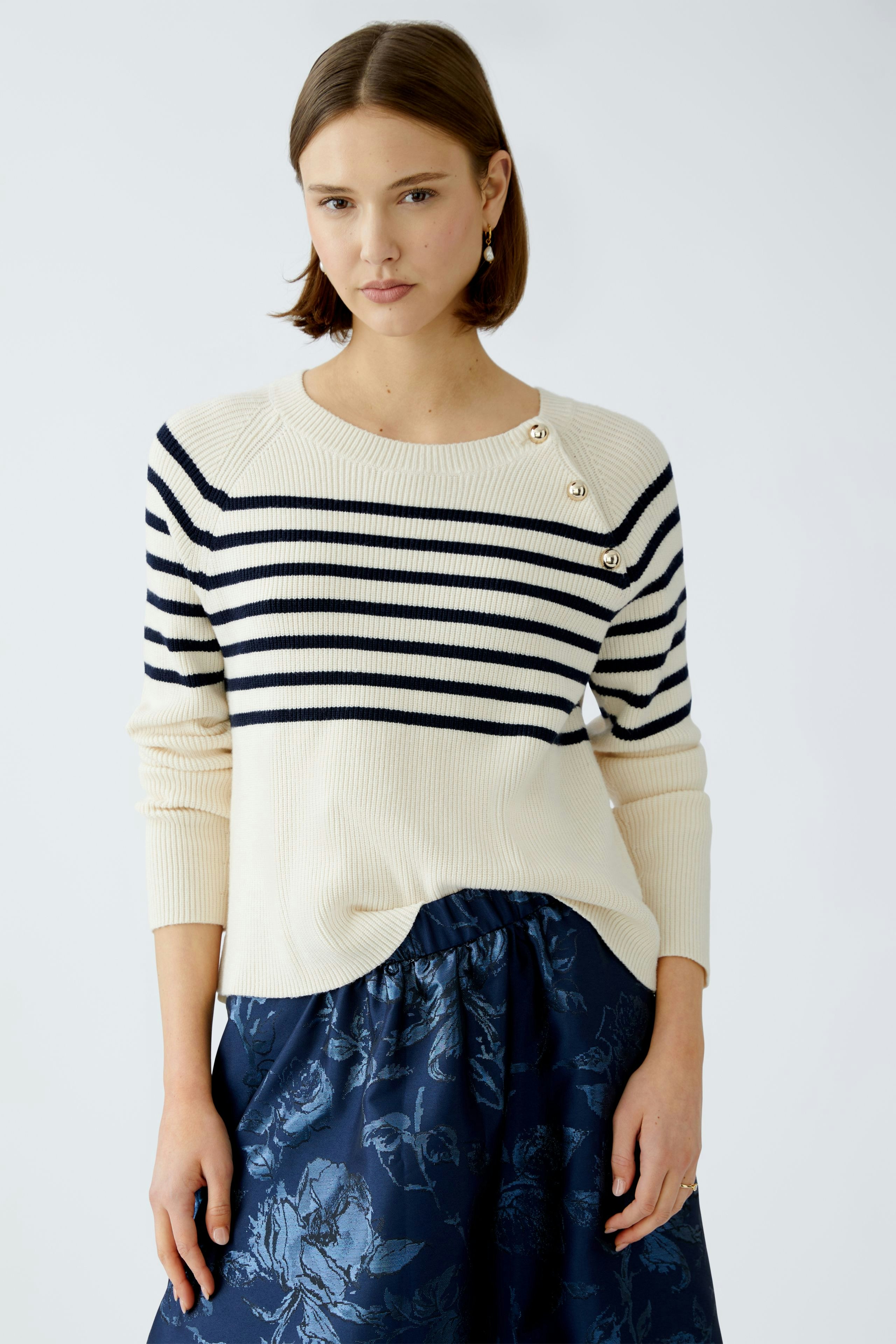 Stylish women's pullover: A woman in a cream and navy striped pullover with decorative buttons.
