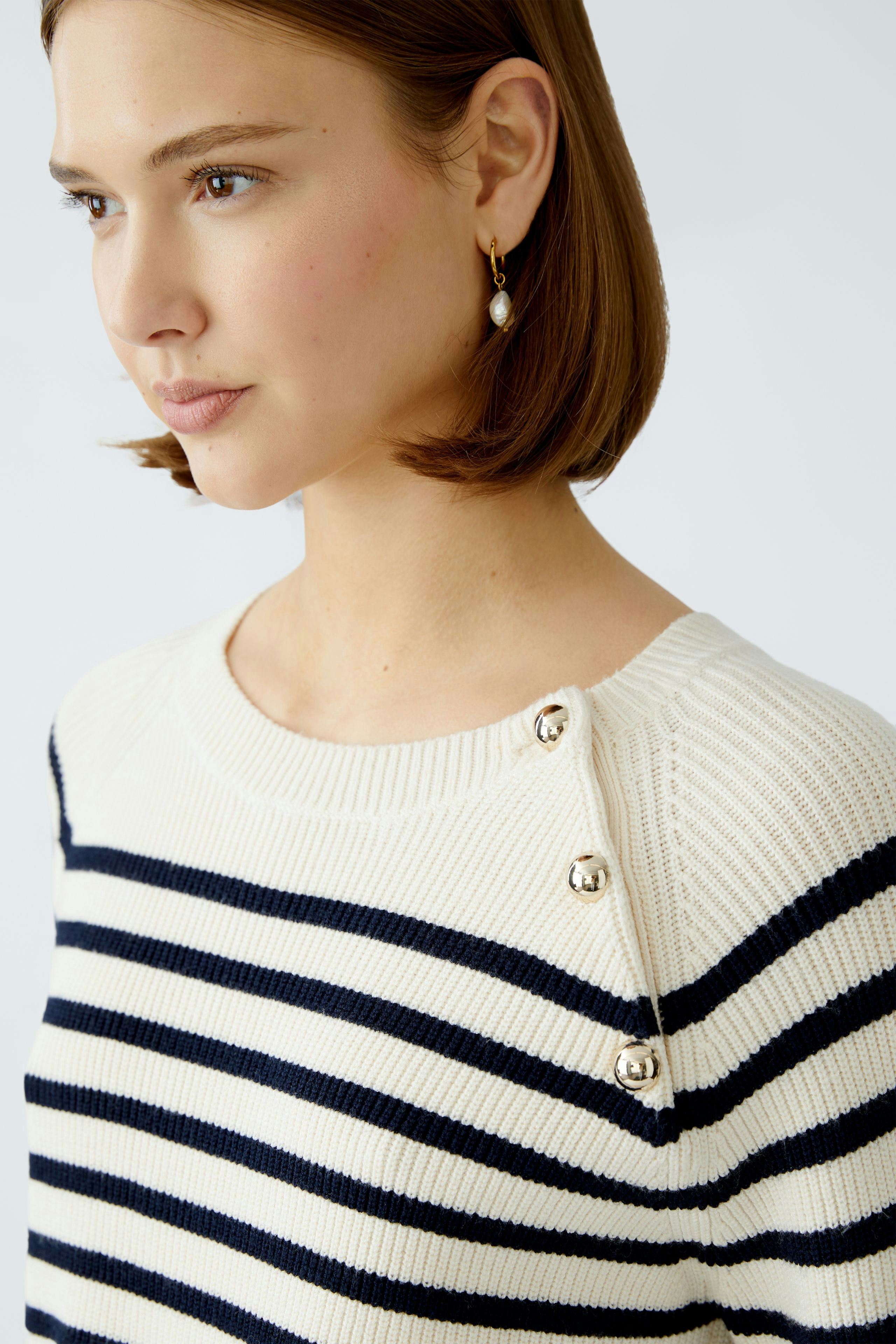 Stylish women's pullover: A woman in a cream and navy striped pullover with button details.