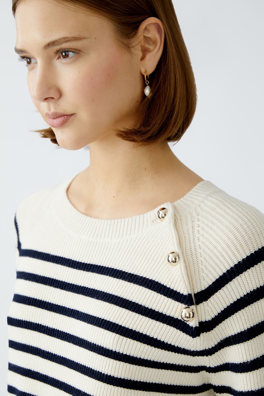 Damen-Pullover: Frau mit gestreiftem Pullover in Creme und Marine, elegante Knöpfe an der Schulter.