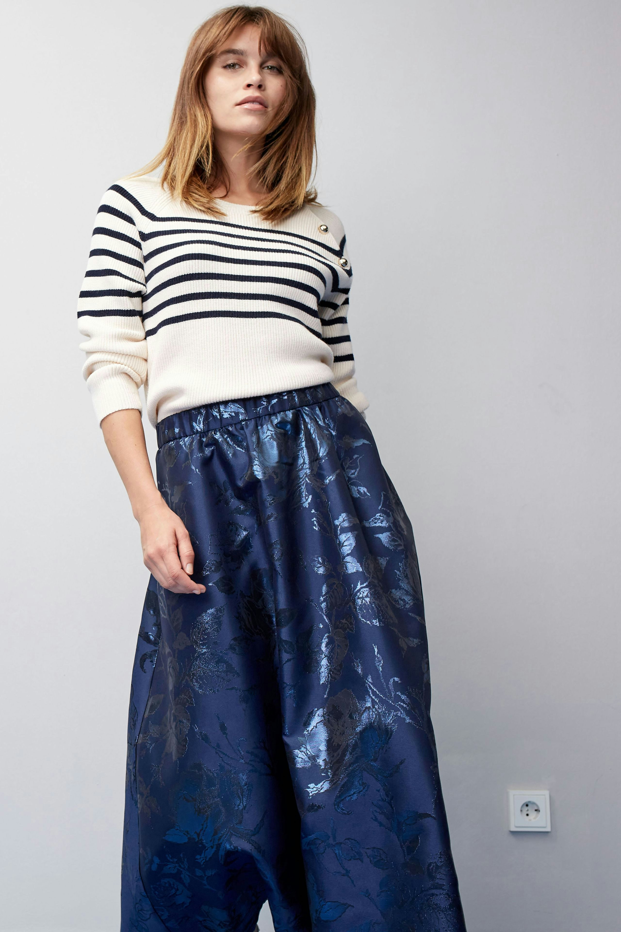 Stylish women's pullover: A woman in a striped pullover paired with a flowy, shiny skirt.