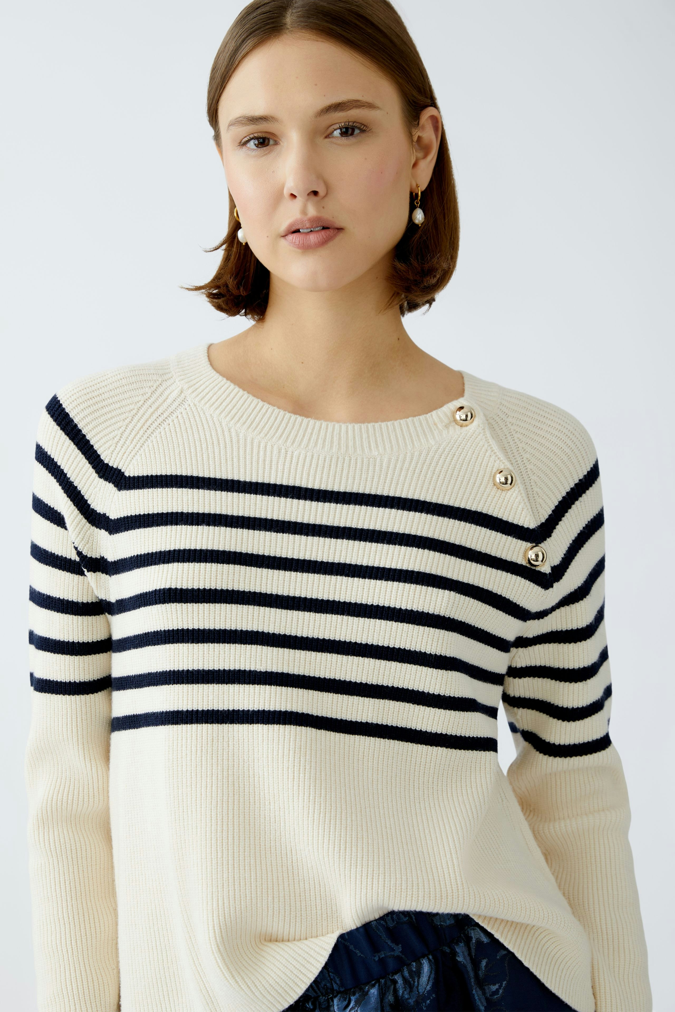 Stylish women's pullover: A woman in a cream and navy striped pullover with button details.