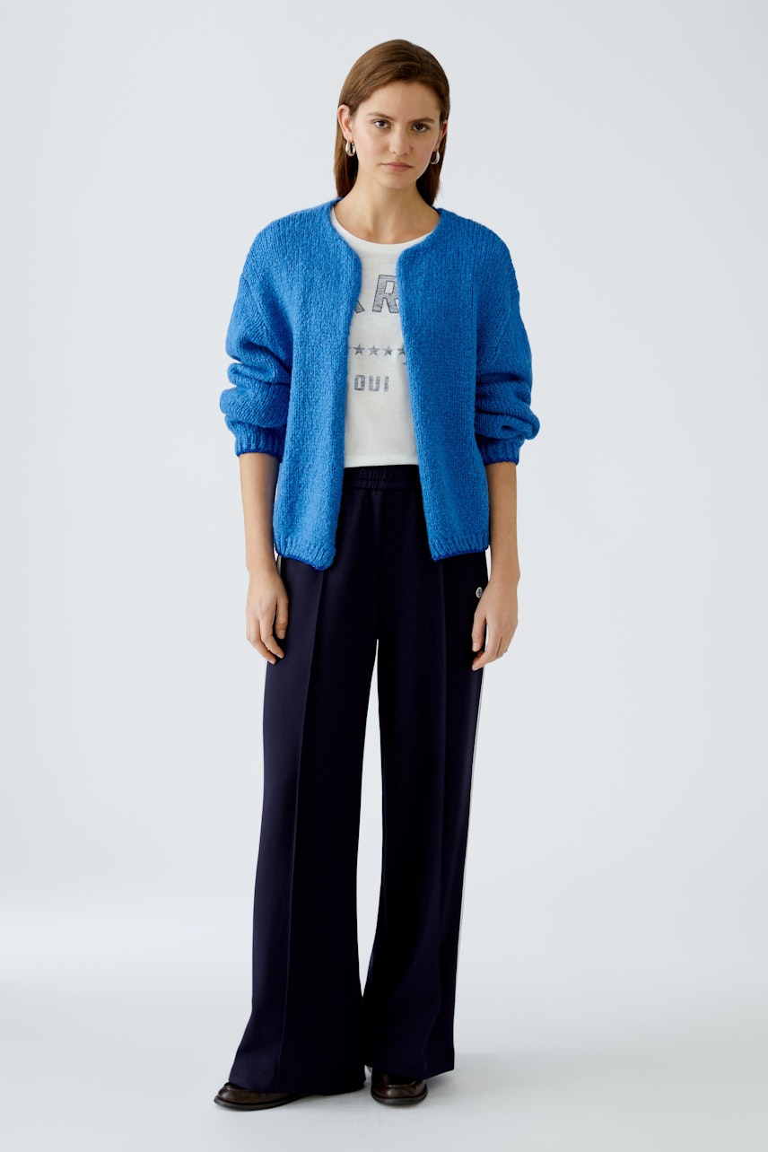 Stylish women's cardigan: A woman in a vibrant blue cardigan over a white top and dark pants.