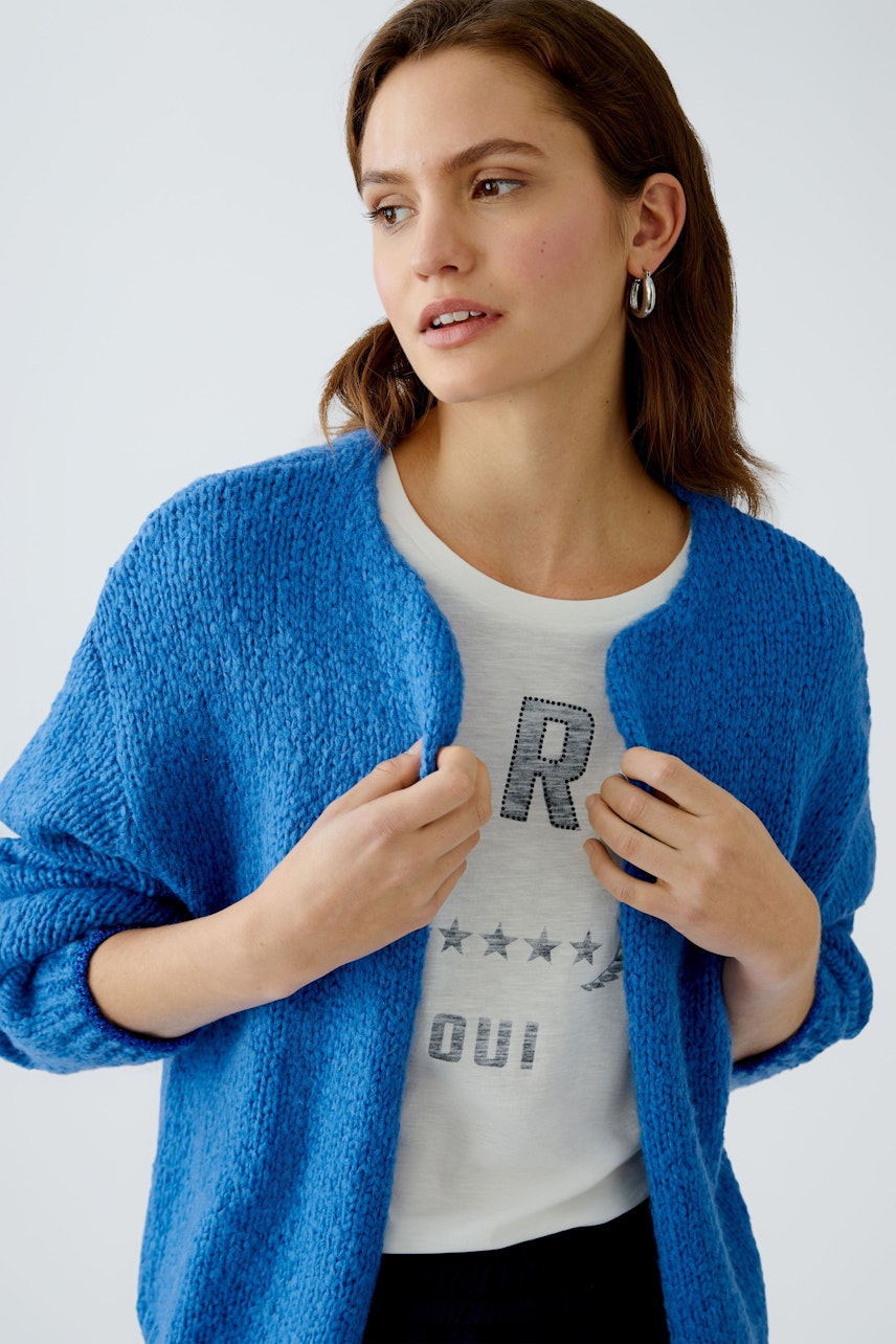 Stylish women's cardigan: A woman in a vibrant blue cardigan over a graphic tee, exuding casual elegance.