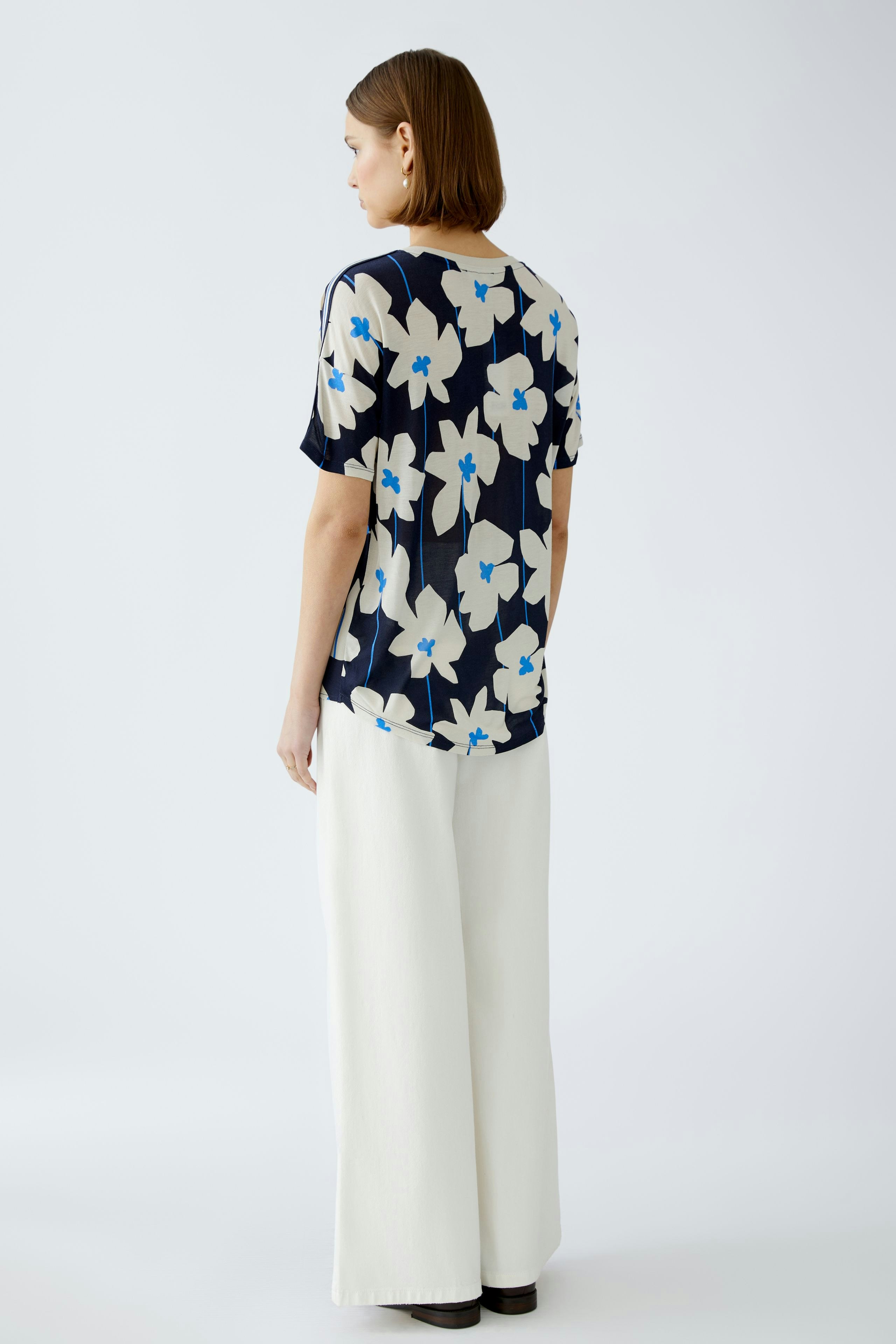 Blusenshirt: Frau trägt ein florales, navyfarbenes Blusenshirt mit kurzen Ärmeln und lässiger Passform.