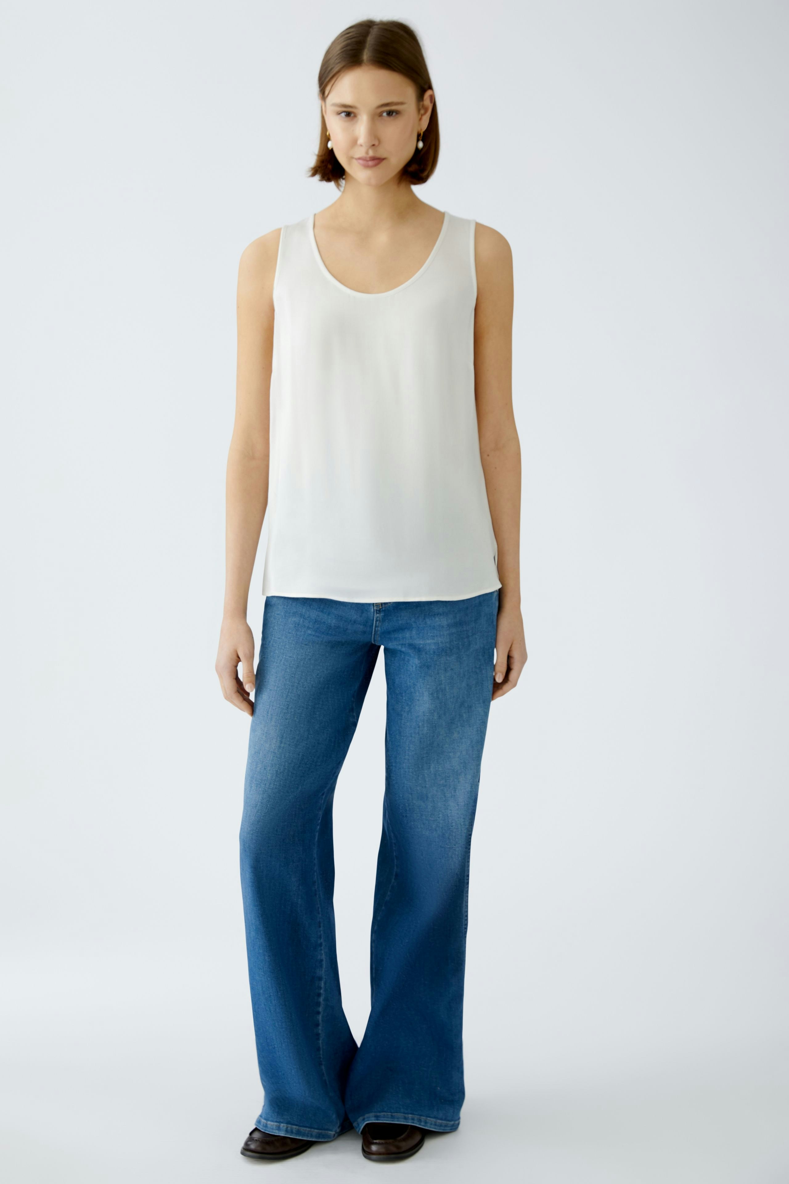 Elegant women's top: A woman in a white sleeveless top paired with flared jeans.