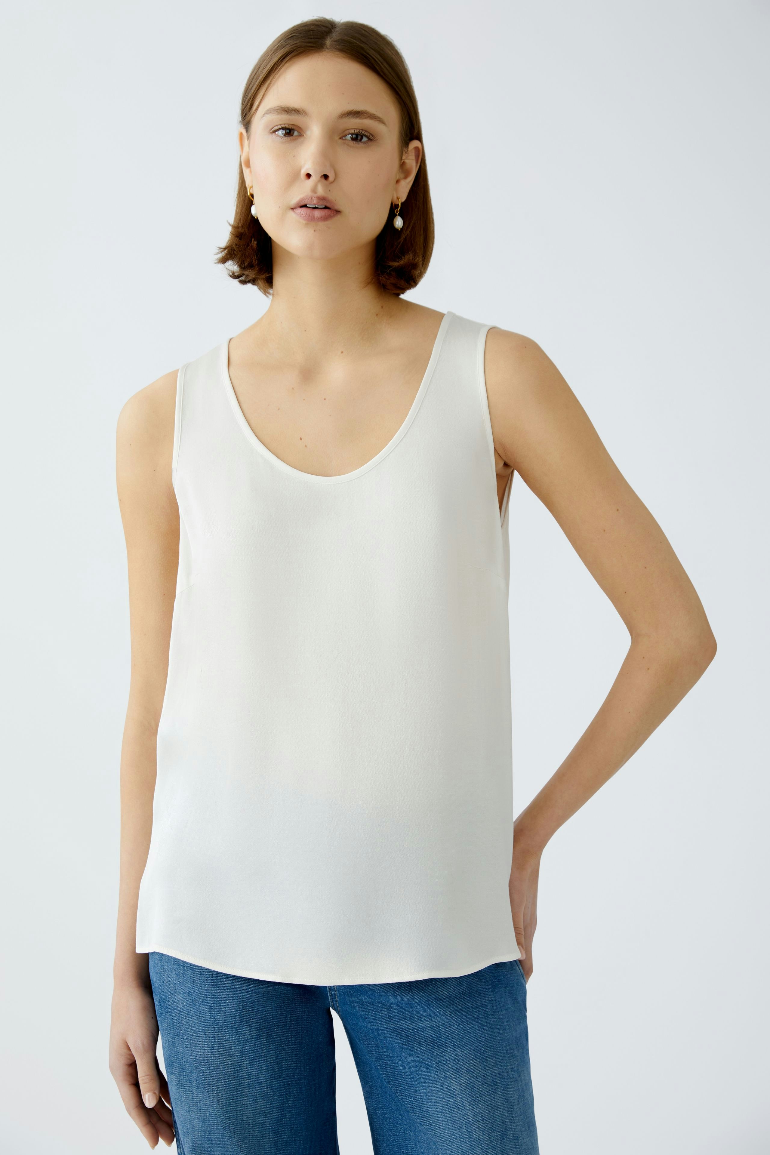Elegant women's top: A woman in a white sleeveless top paired with casual jeans.