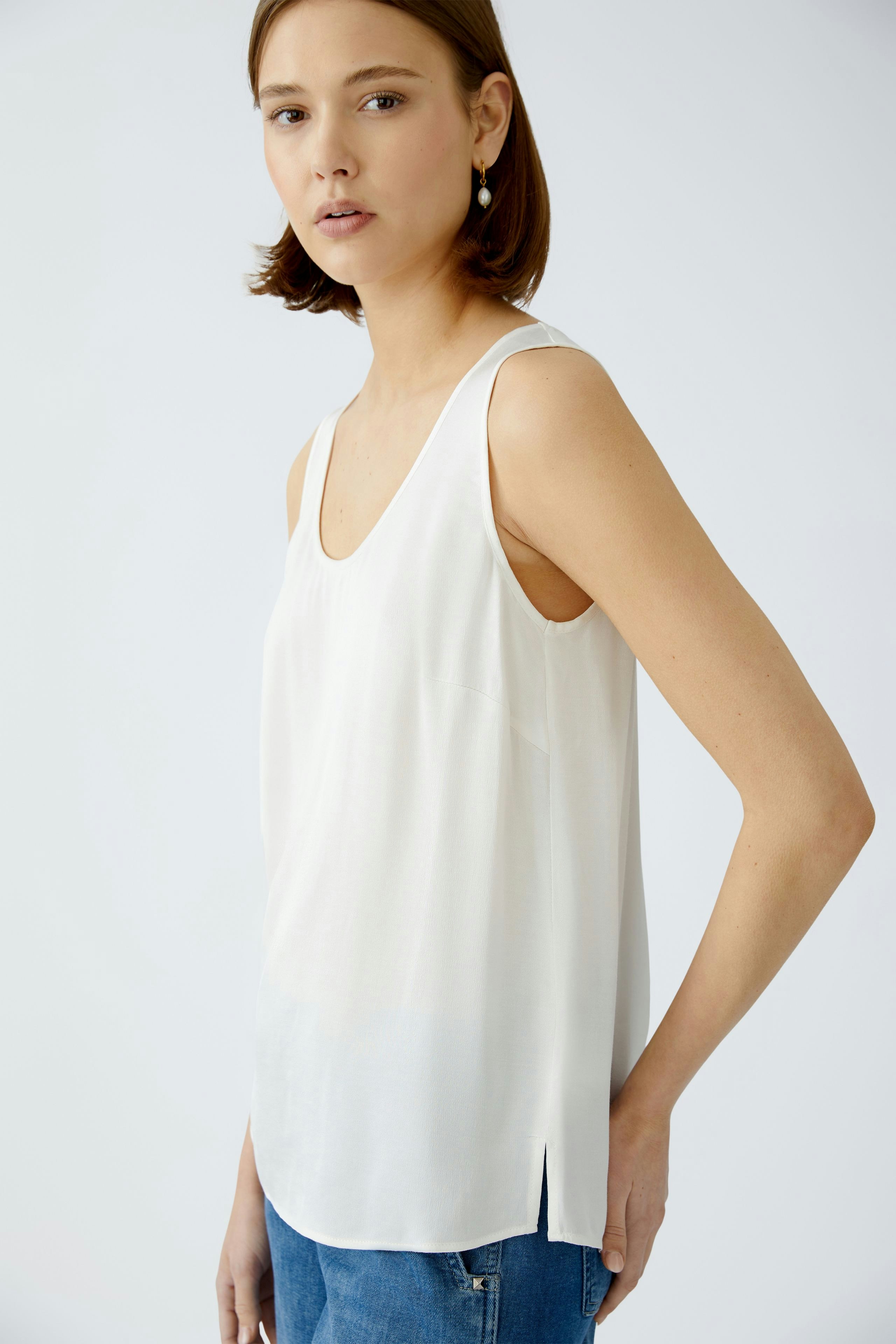 Elegant women's top: A woman in a white sleeveless top paired with casual jeans.