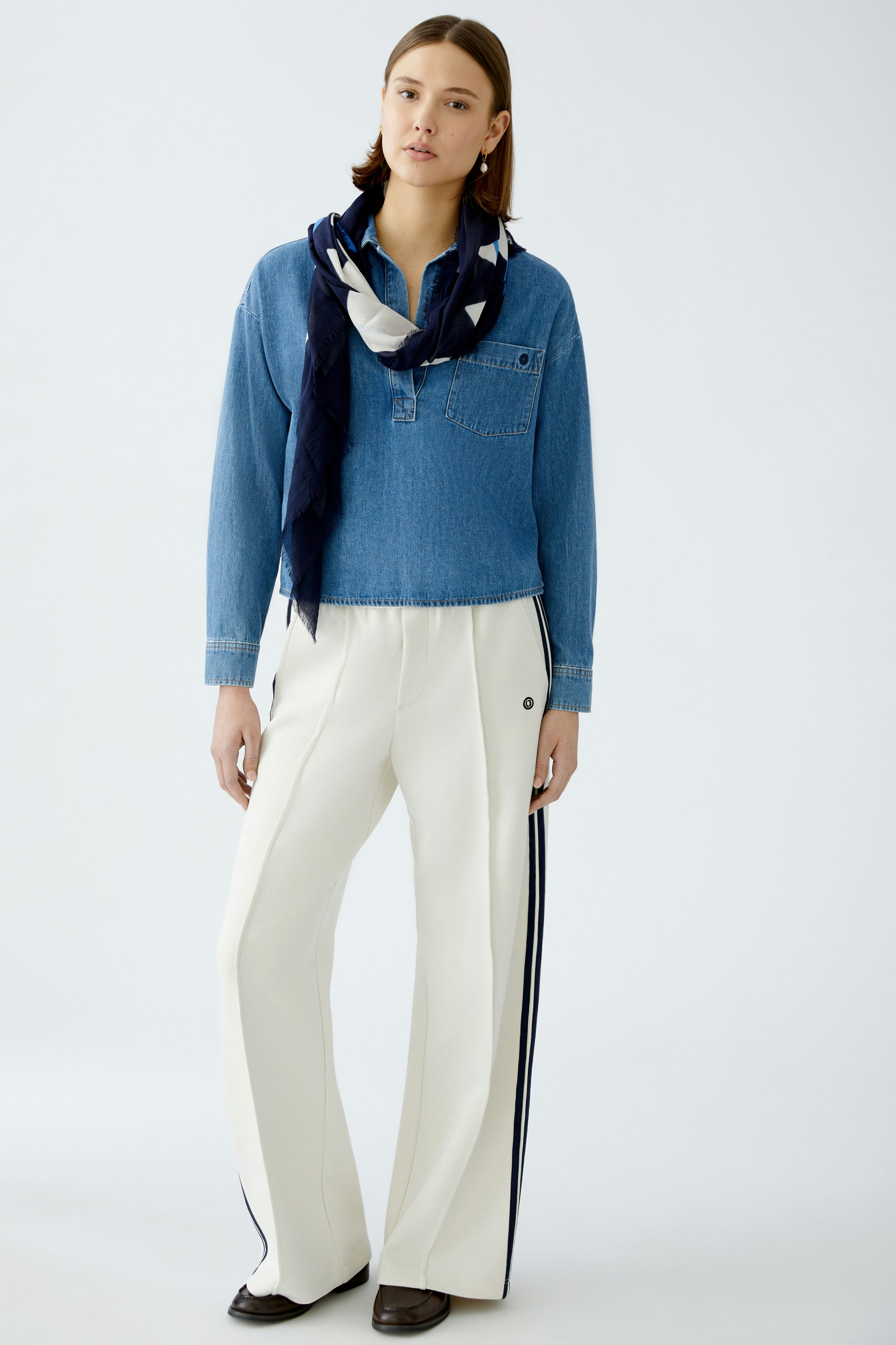 Stylish scarf: A woman wearing a navy scarf with a chic design, paired with a denim shirt and white pants.