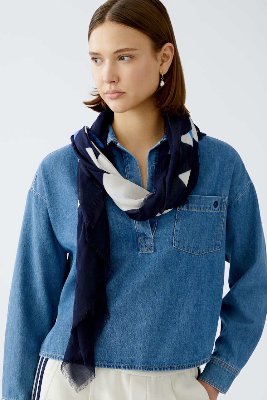 Stylish scarf: Woman wearing a navy scarf with white patterns, paired with a denim shirt.