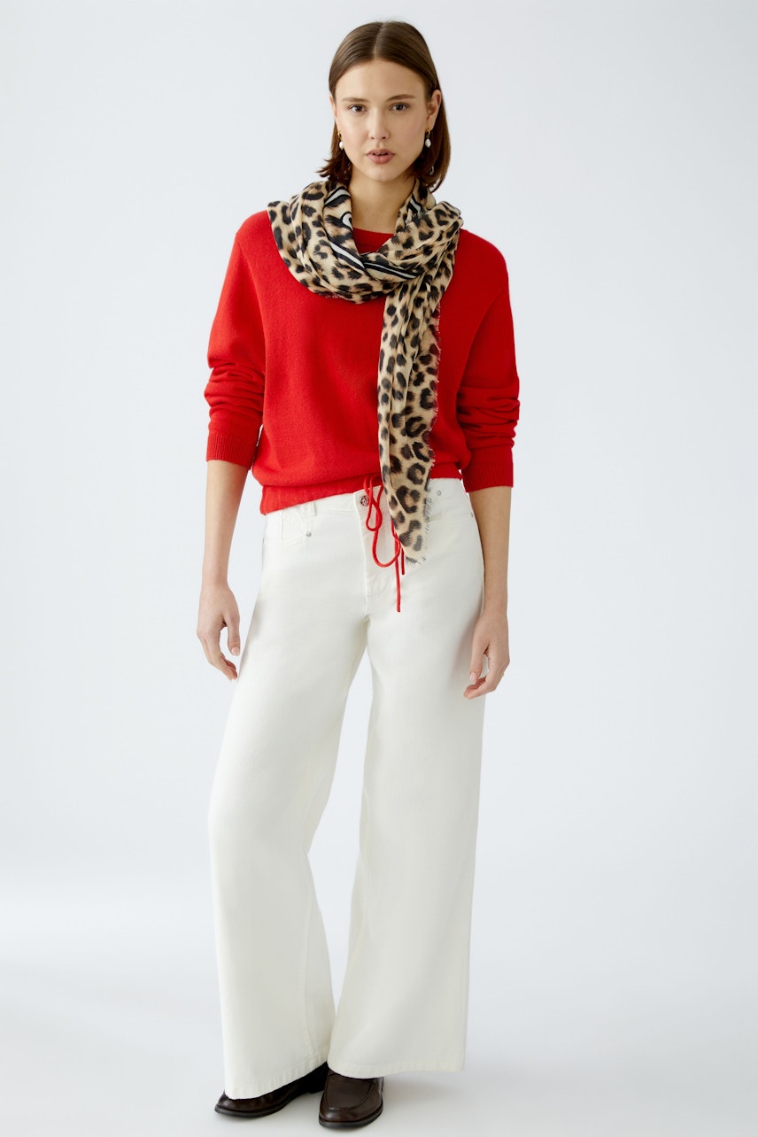 Stylish scarf: A woman wearing a leopard print scarf over a red pullover and white pants.