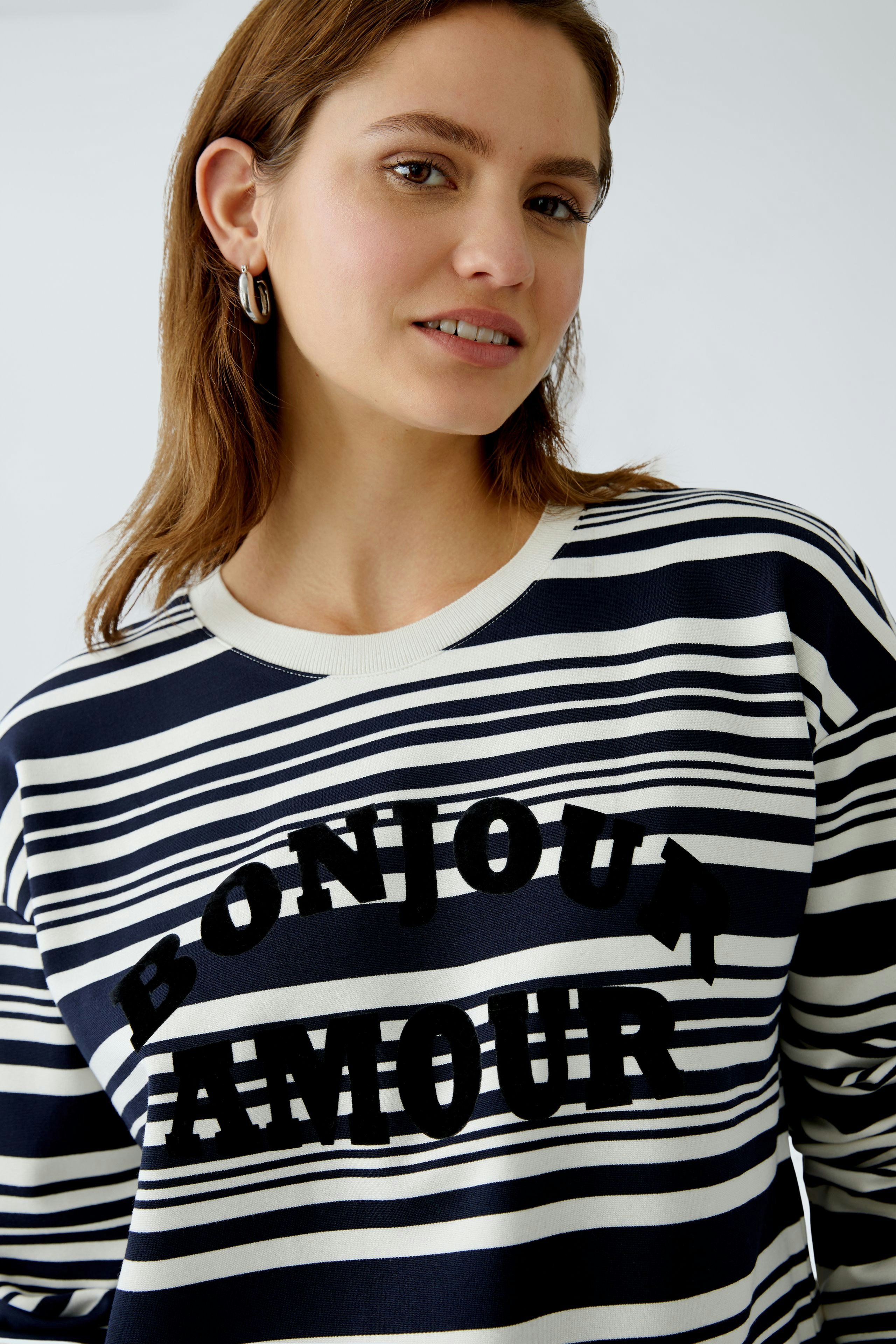 Damen-Sweatshirt: Frau in gestreiftem Pullover mit "BONJOUR AMOUR" Schriftzug lächelt freundlich.