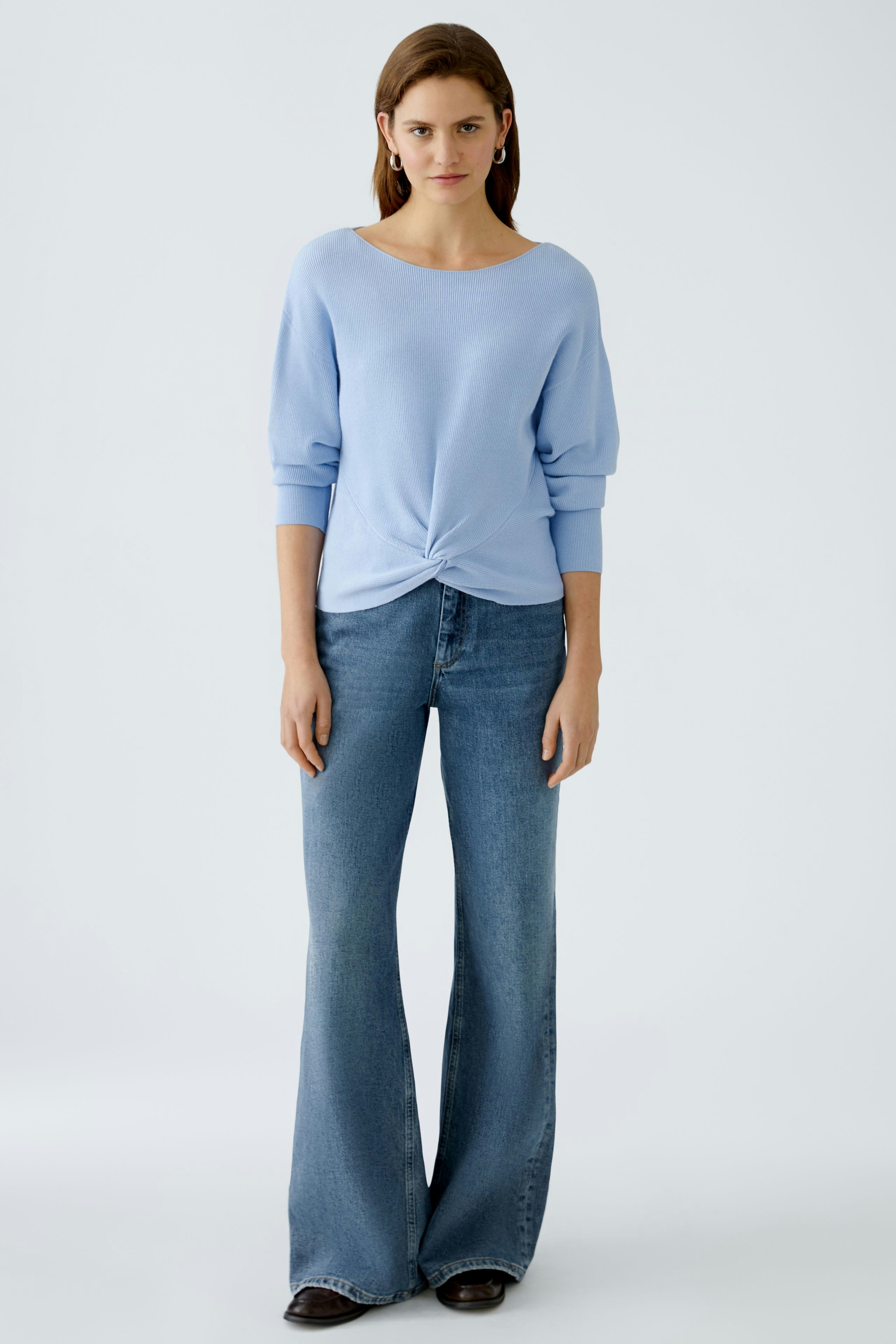 Stylish women's pullover: A woman in a light blue pullover with a knotted front, paired with flared jeans.