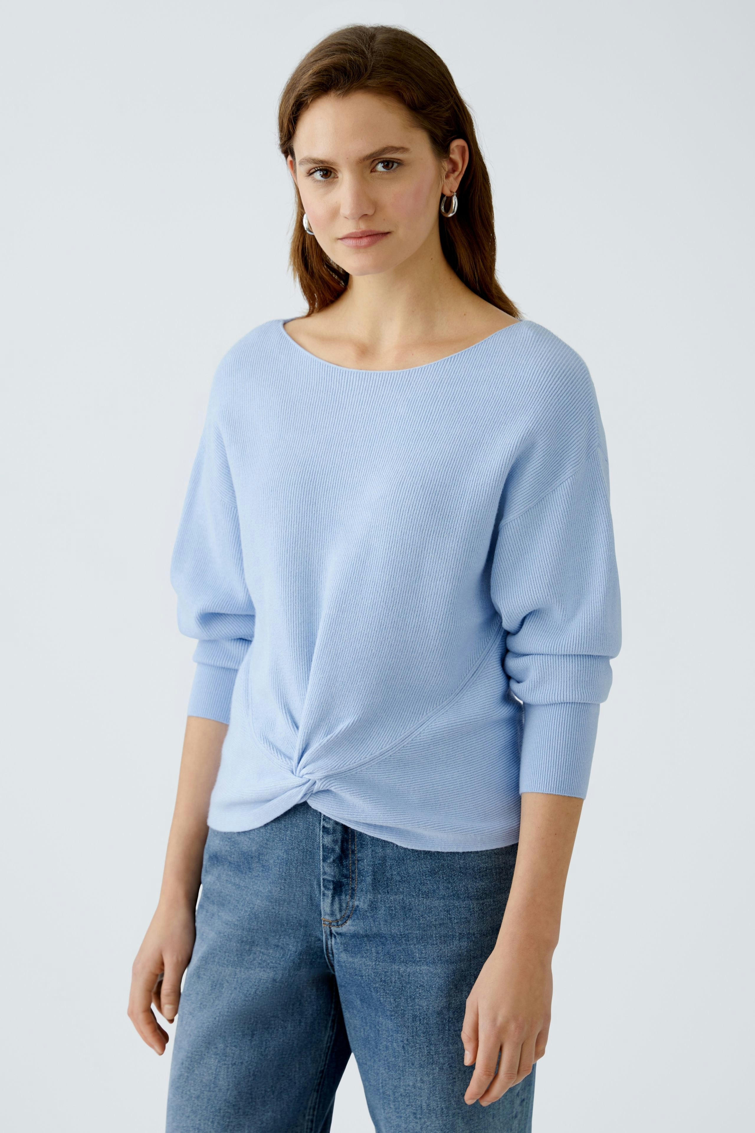 Stylish women's pullover in light blue, featuring a twist front design, paired with casual jeans.