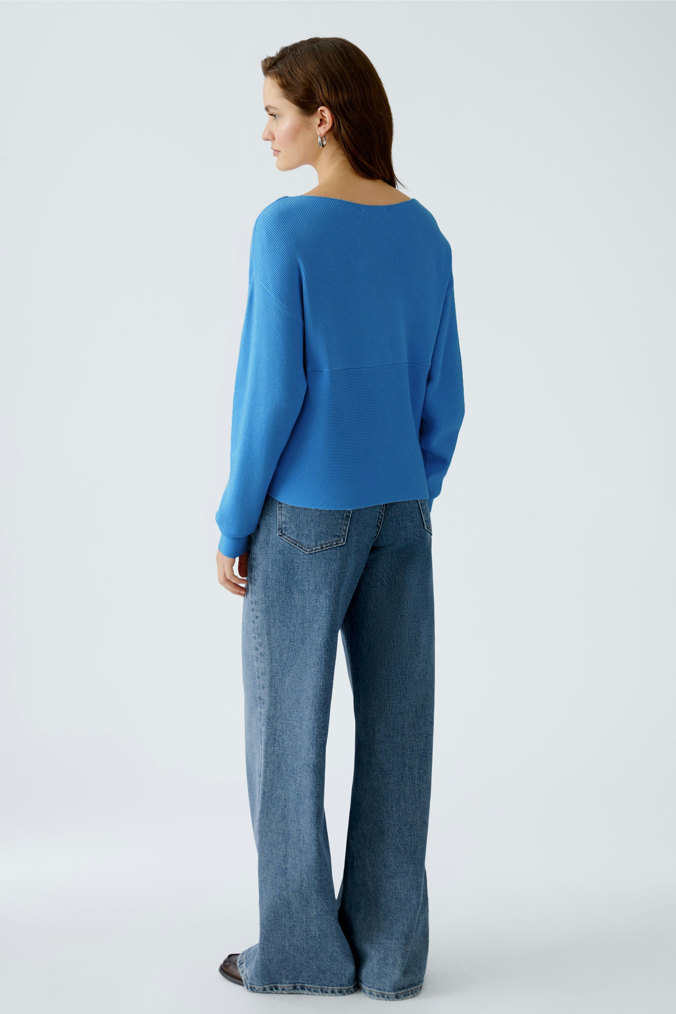 Damen-Pullover: Frau in blauem, lässigem Pullover mit weitem Schnitt und bequemen Jeans.