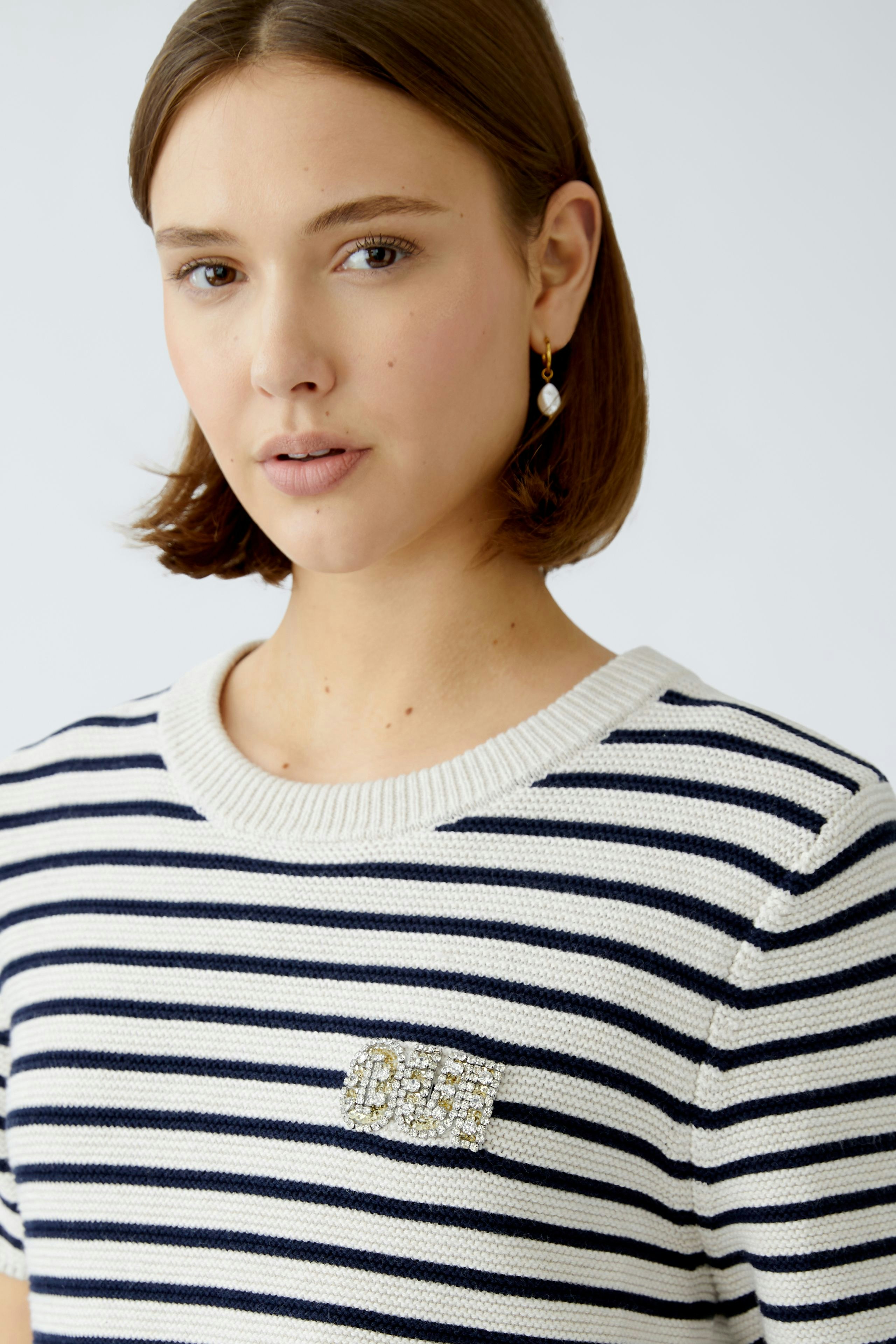 Stylish women's pullover: A woman in a striped pullover with a decorative logo, exuding casual elegance.