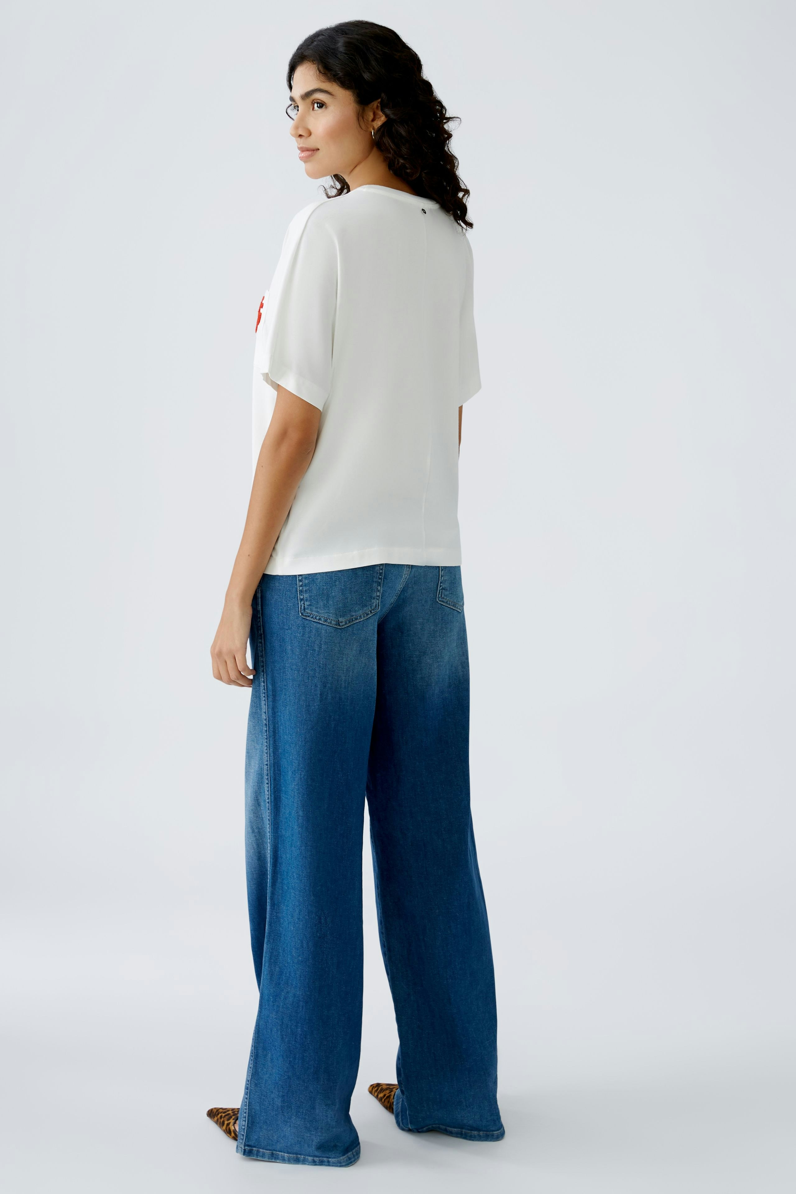 Elegantes Damen-T-Shirt: Frau in weißem T-Shirt mit lässigem Schnitt und weiten Jeans.