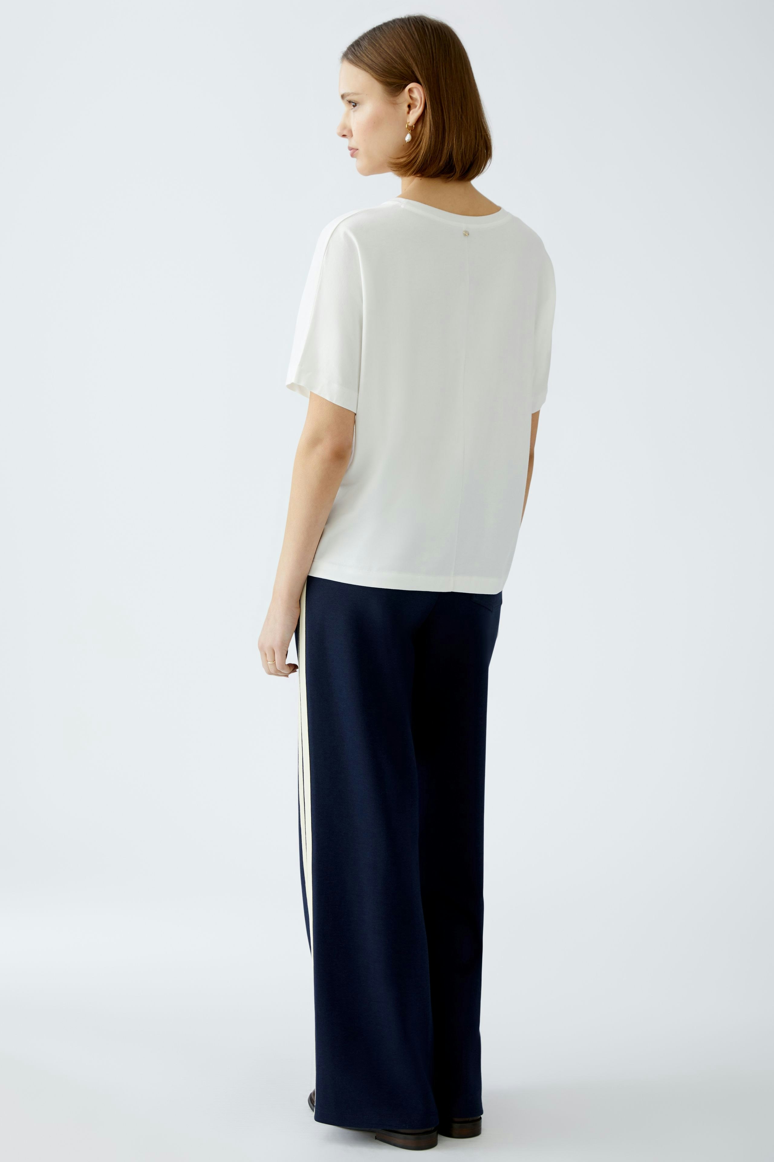 Elegantes Damen-T-Shirt: Frau in weißem T-Shirt mit lässigem Schnitt und schlichten Details von hinten.