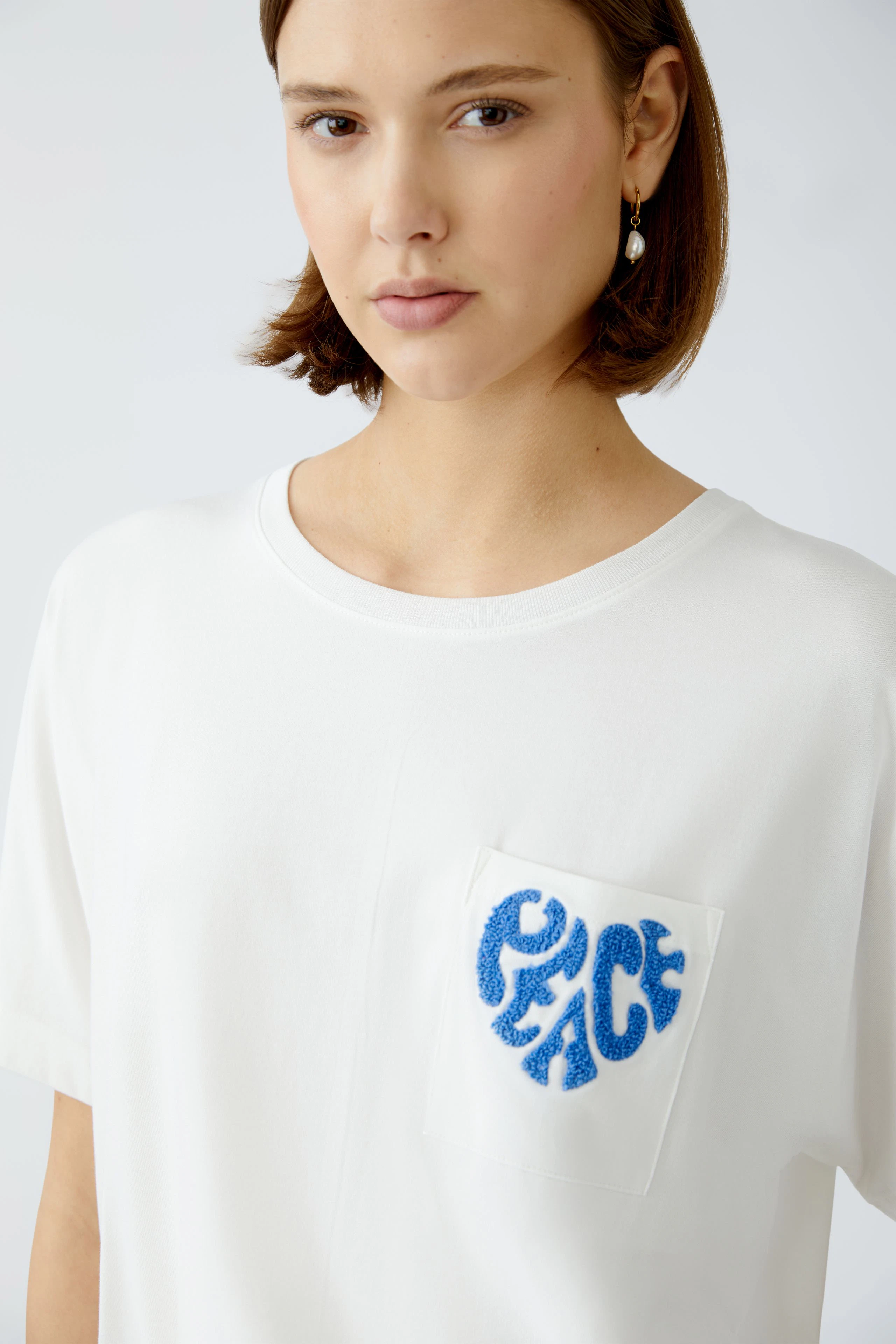 Damen-T-Shirt: Junge Frau trägt ein weißes T-Shirt mit blauem Peace-Logo auf der Brust.