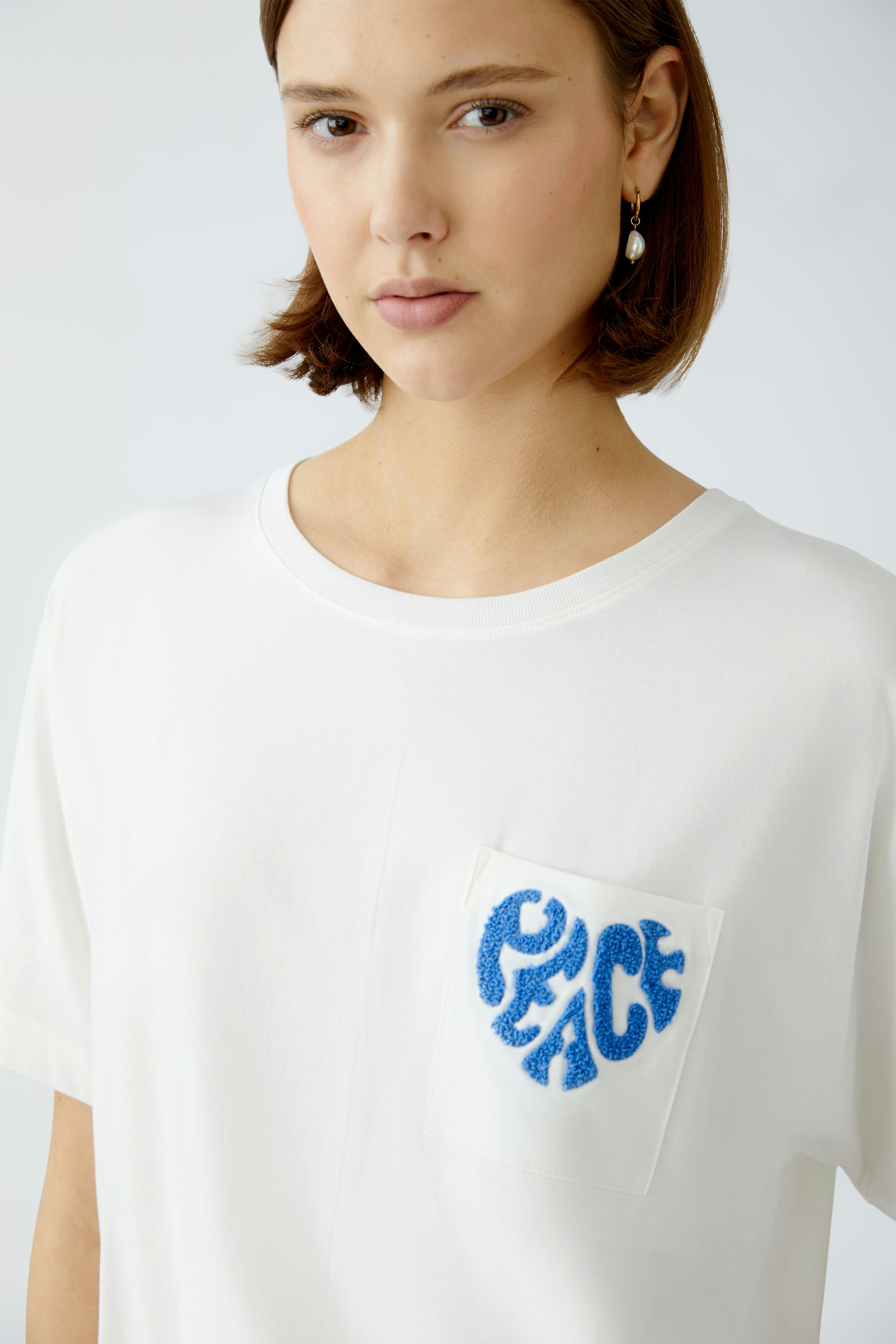 Damen-T-Shirt: Junge Frau trägt ein weißes T-Shirt mit blauem Peace-Logo auf der Brust.