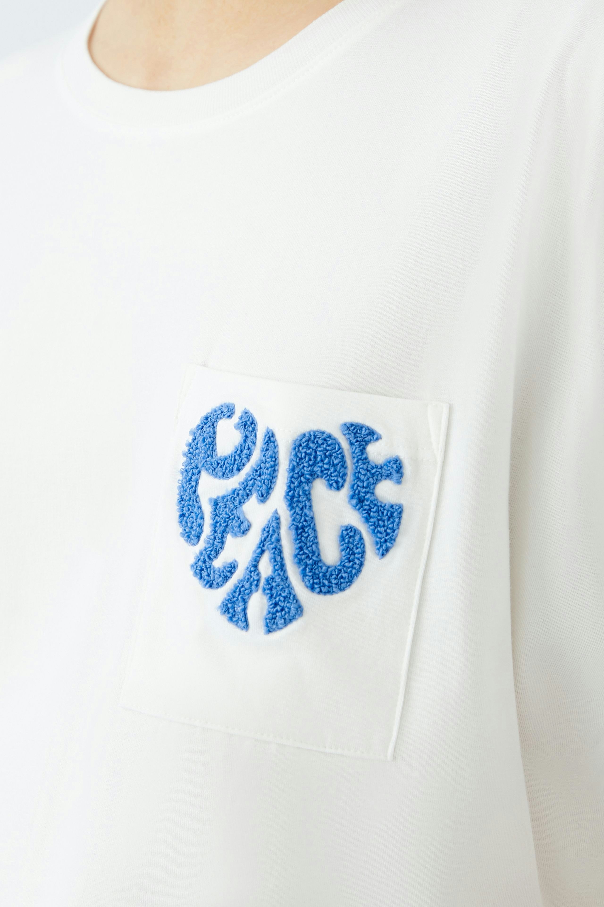 Weißes Damen-T-Shirt mit blauem Peace-Logo auf der Brust, lässig und modern.