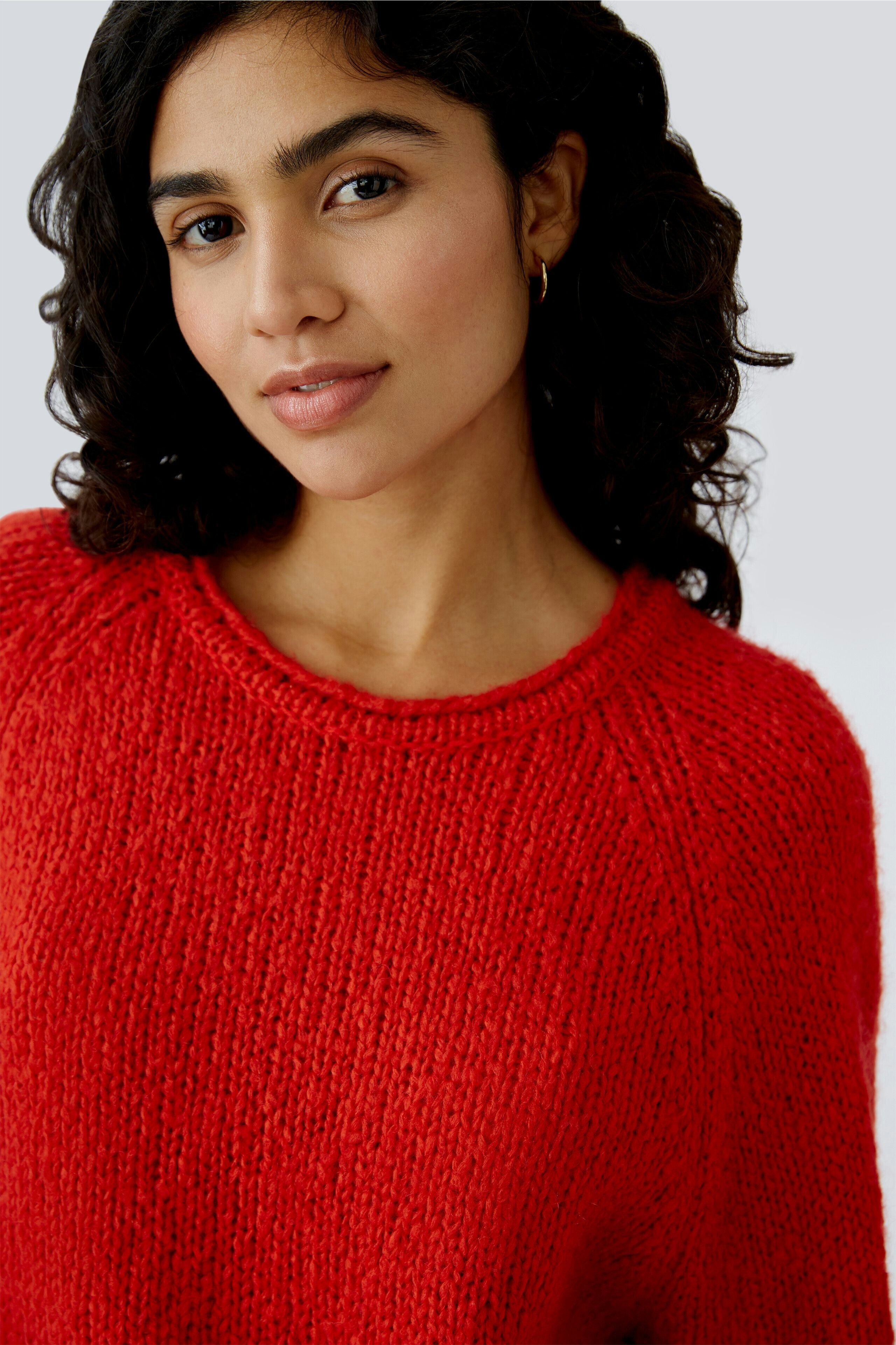 Roter Damen-Pullover: Frau mit lockigem Haar trägt einen lässigen, strukturierten Pullover.
